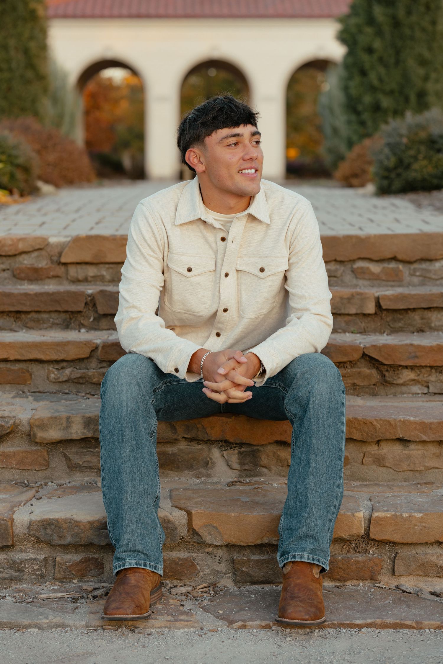 Person in light denim jacket sitting on stone steps with autumn scenery behind.