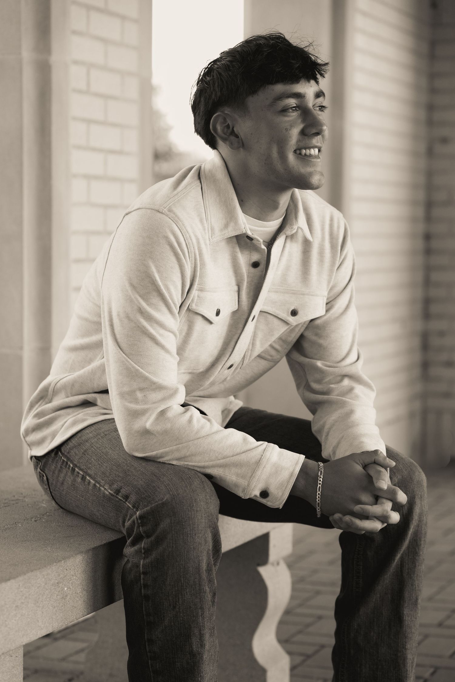 A monochrome image of someone seated on steps wearing a light jacket and dark jeans.