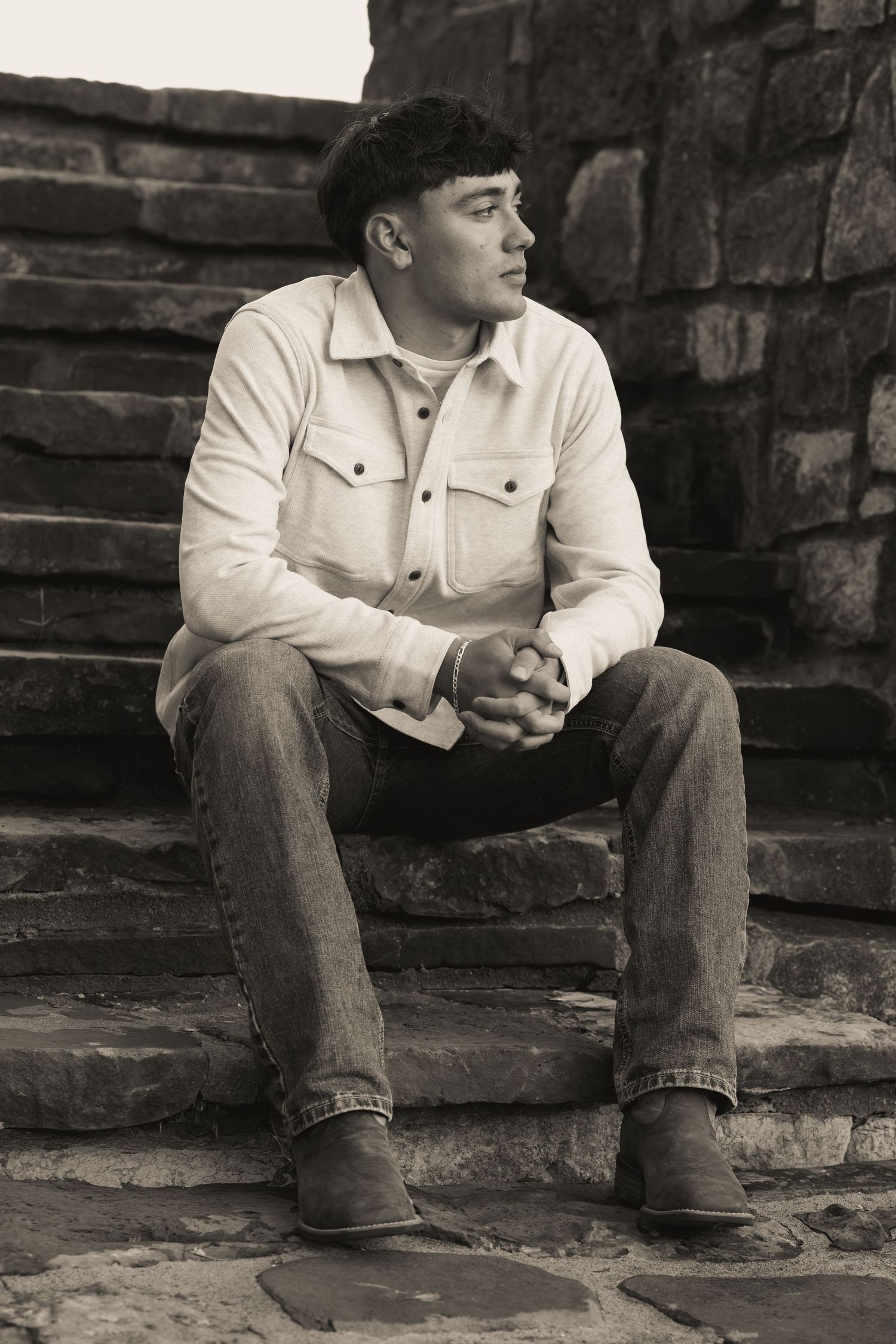 Black and white image of someone seated on stone steps in casual attire.
