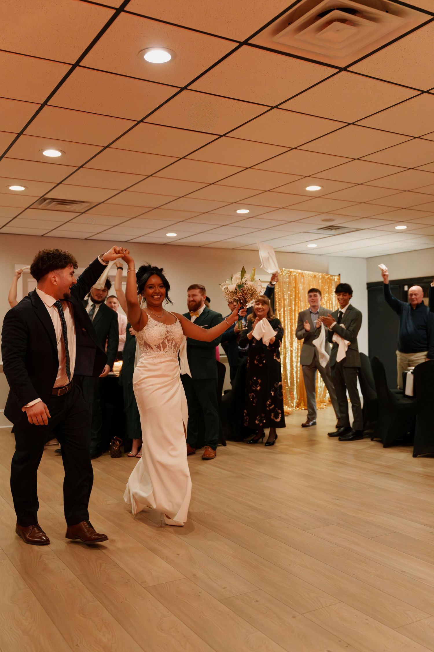 Wedding guests celebrate as a couple dances together on a wooden floor during their reception.
