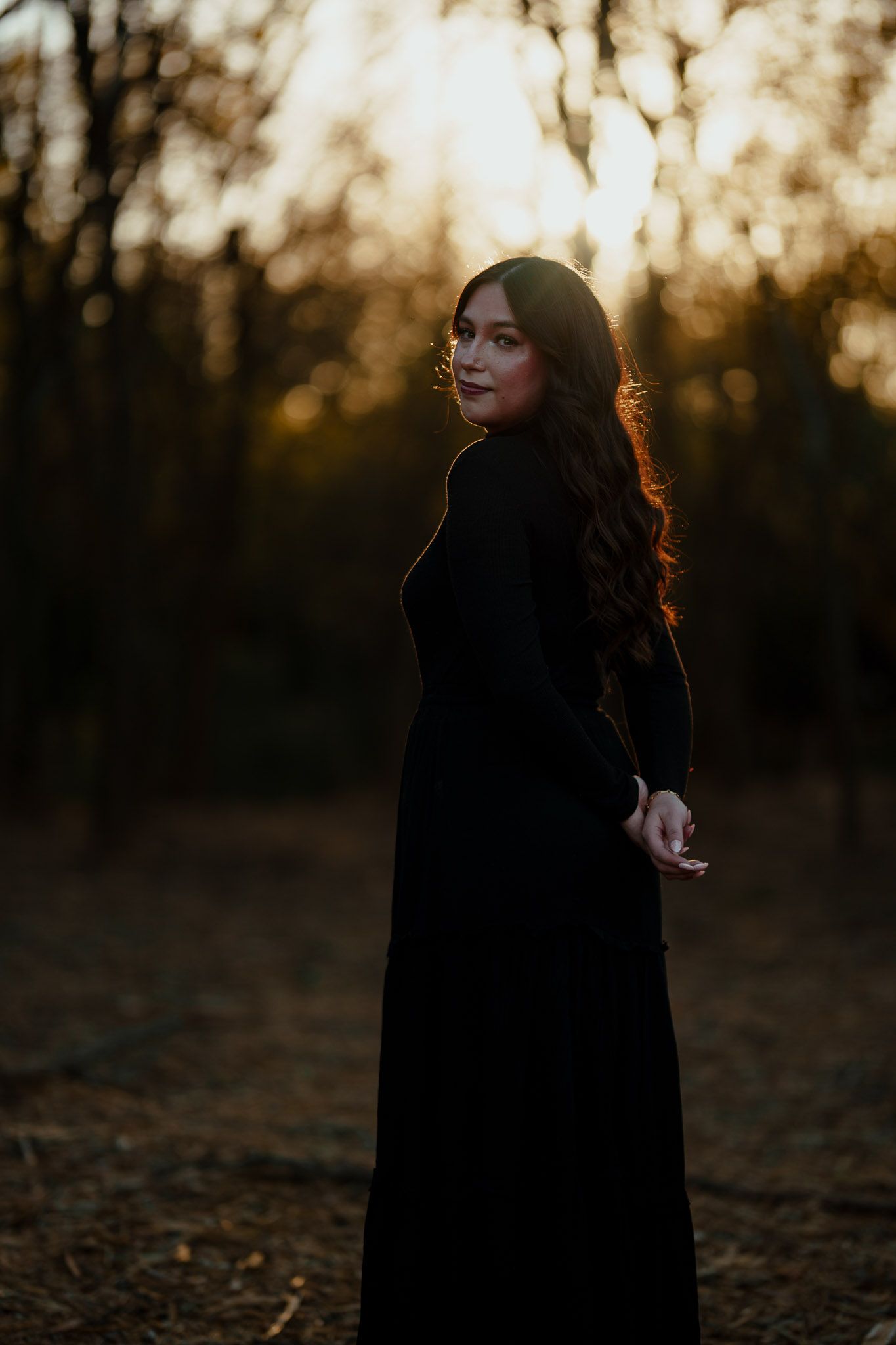 Artistic silhouette photo of figure in black dress against sunset in forest.