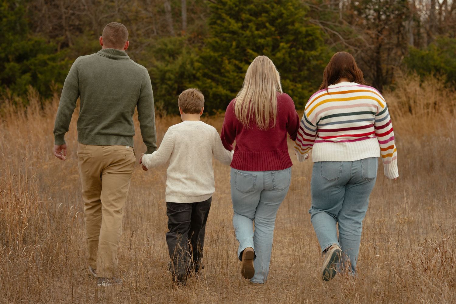 Family members walk away from camera through tall grass during golden hour.