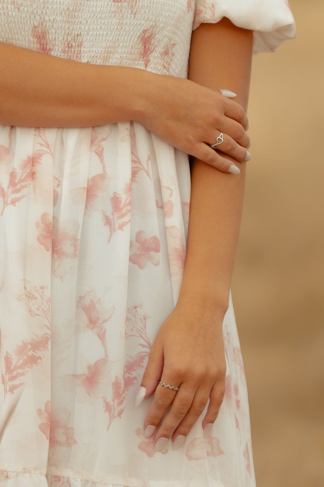 Close-up of hands wearing an engagement ring against a white floral dress.