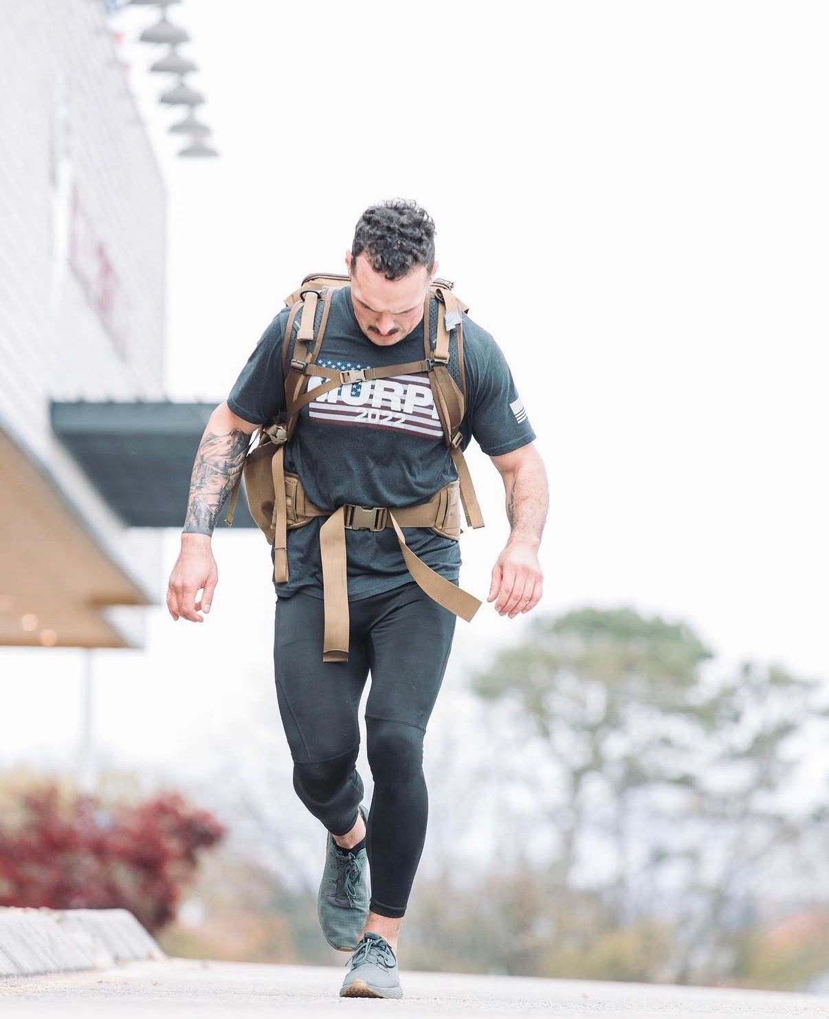 Person in black athletic wear and tactical vest climbing concrete steps during an outdoor training workout.