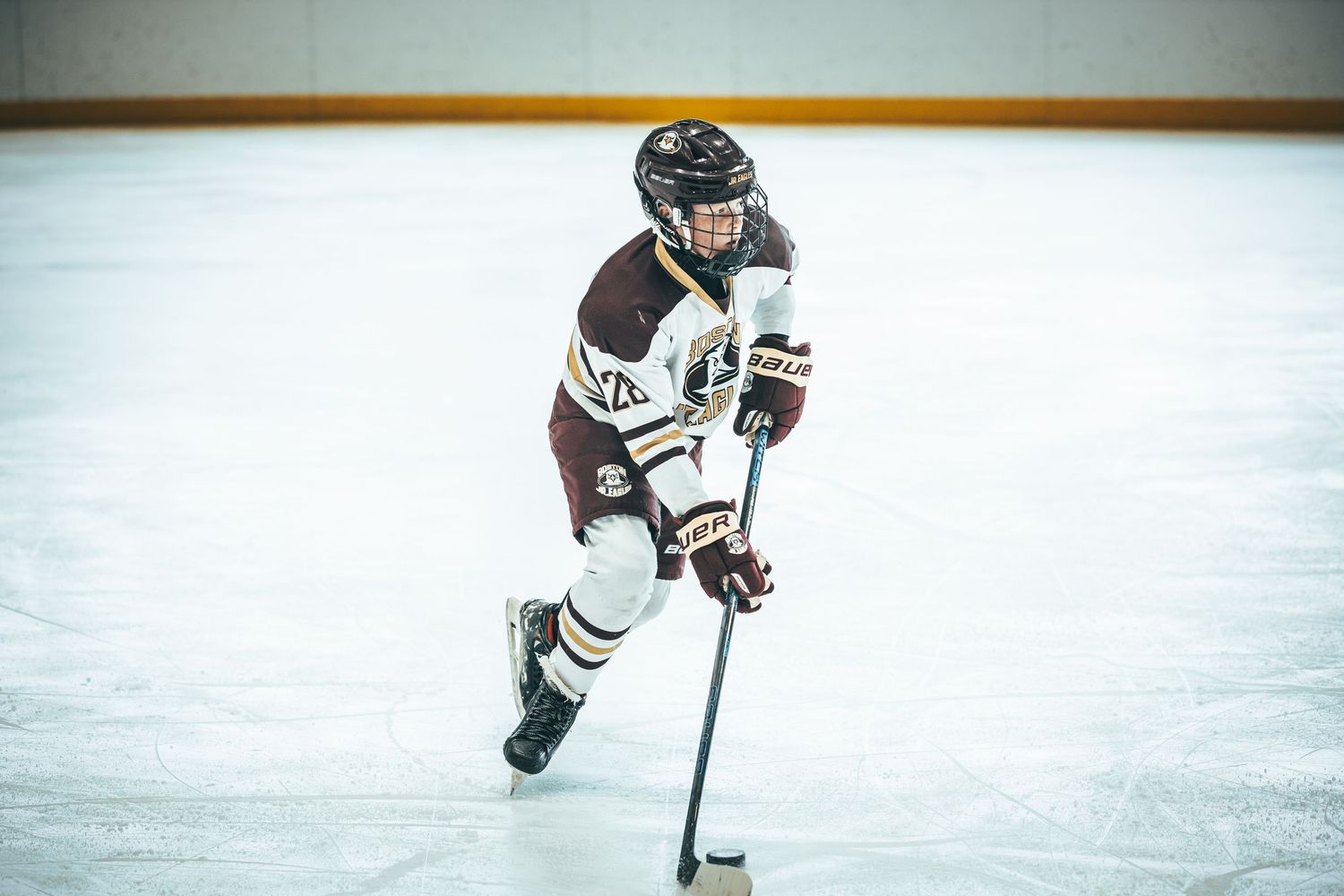 Ice hockey player in maroon jersey skates with puck during competitive match on indoor rink.
