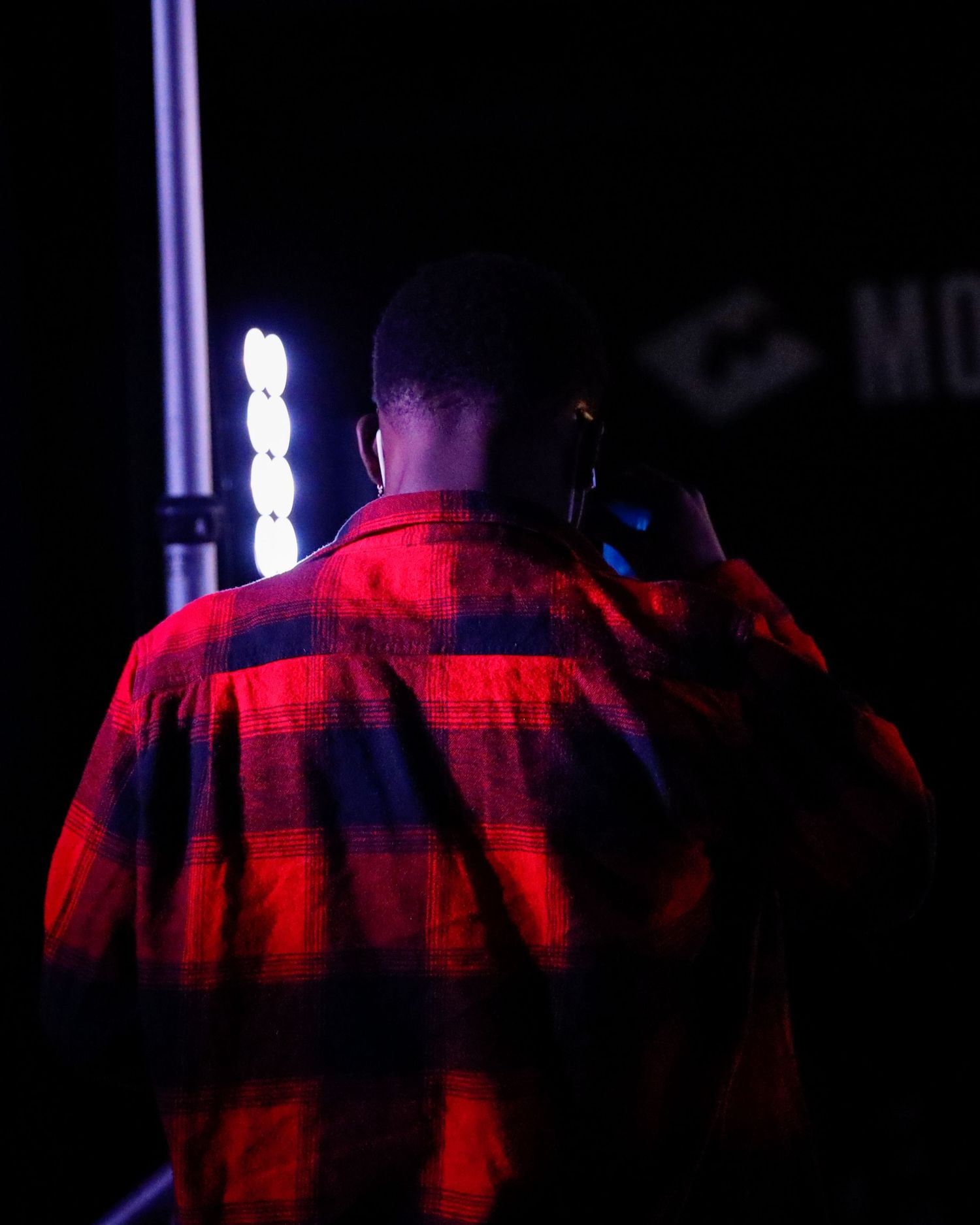 A person in a plaid shirt illuminated by dramatic red and blue lighting on a dark stage.