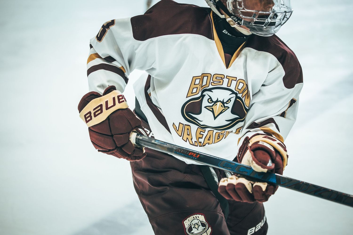 Hockey player in brown and white uniform skates on ice while handling puck during competitive game.