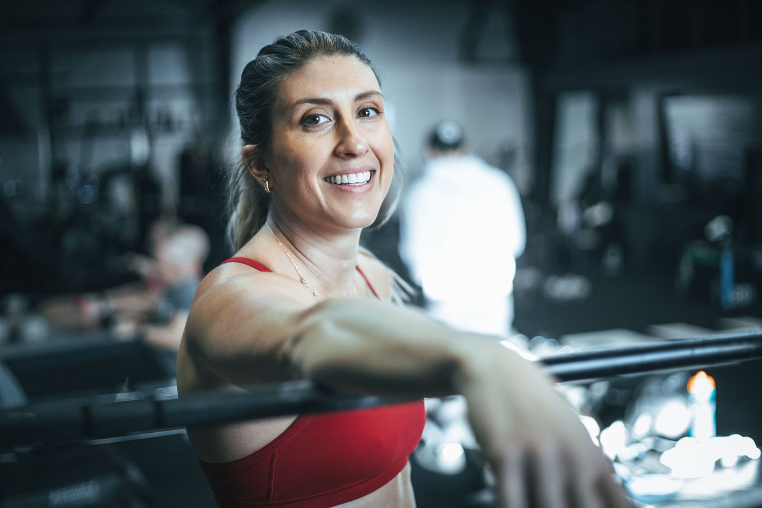 Person in red workout top smiling while exercising at a modern fitness facility.