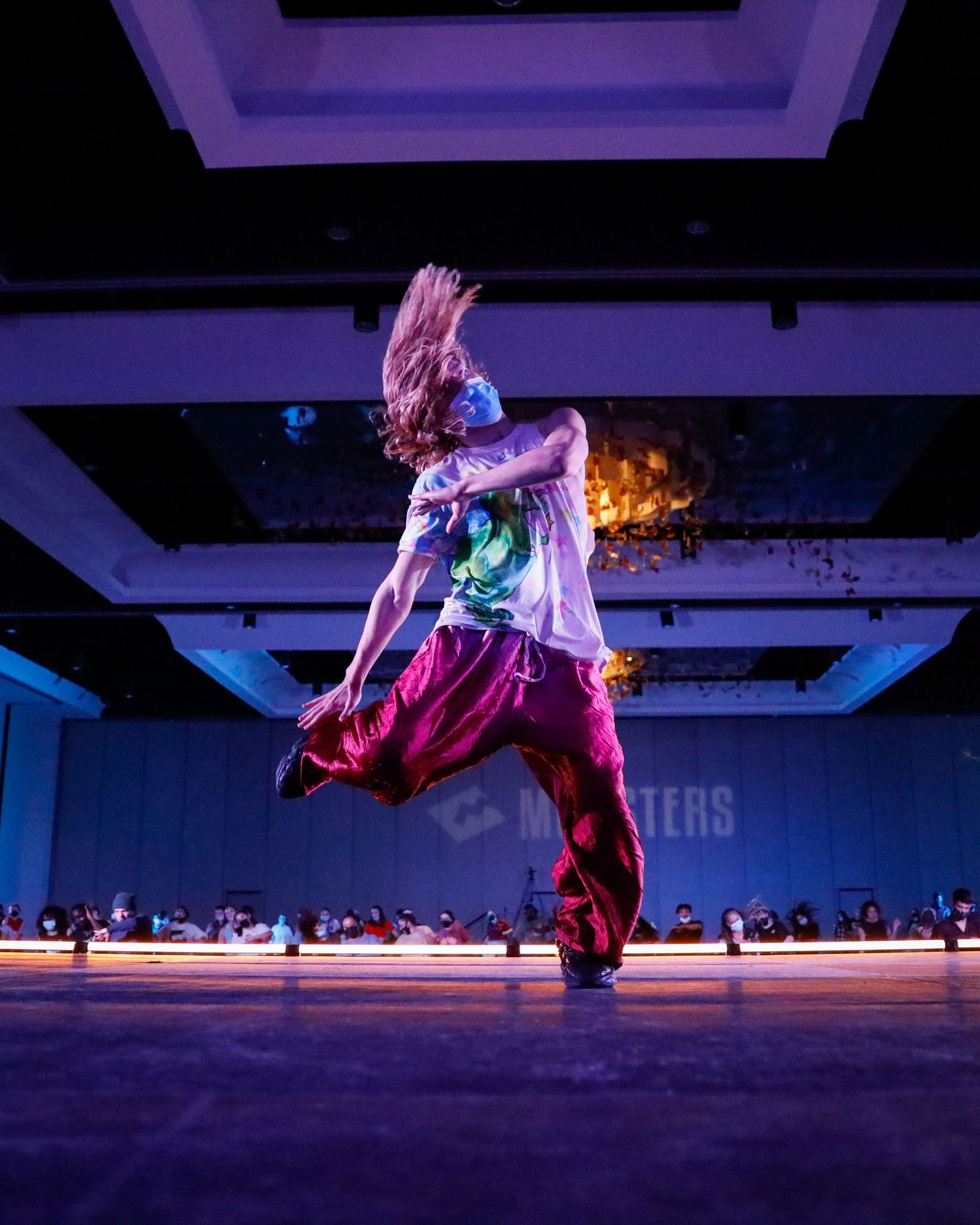 A dynamic dance performance sequence showing leaps and movements illuminated by colorful purple and blue stage lighting.