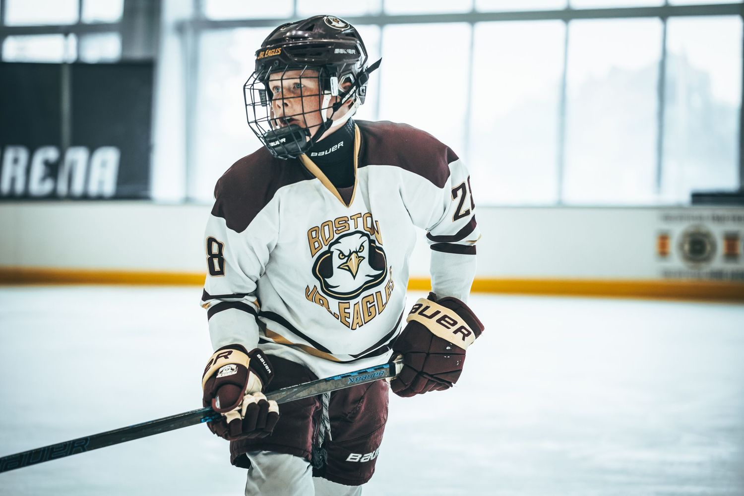 Hockey player in white and brown jersey skates with stick raised during competitive game on indoor rink.