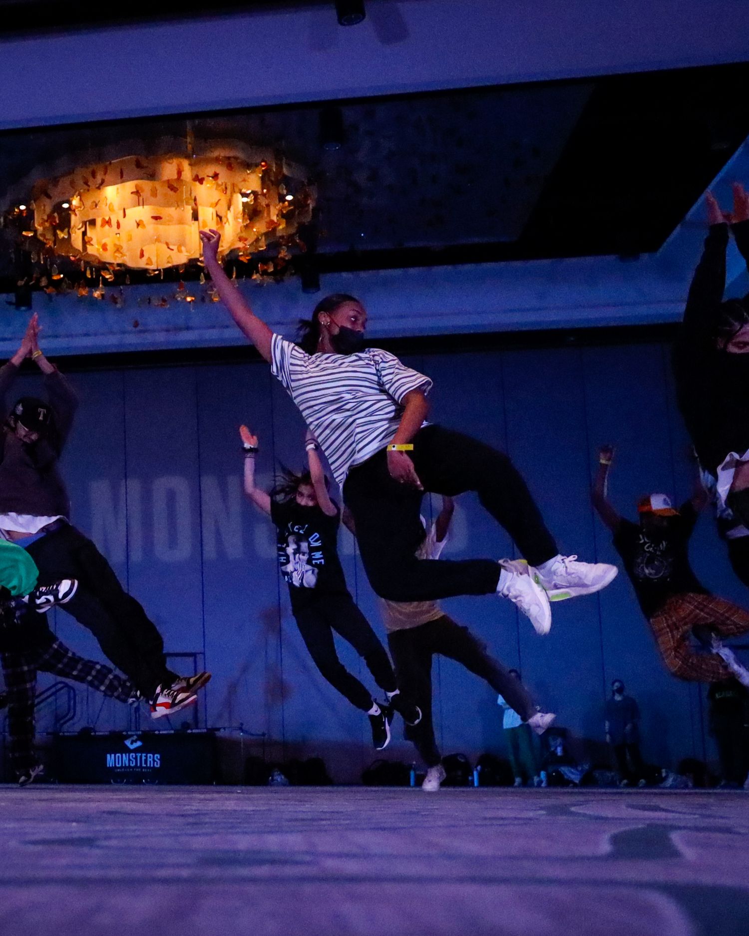 Dancers perform dynamic breakdancing moves on a dimly lit stage with dramatic lighting and shadows.