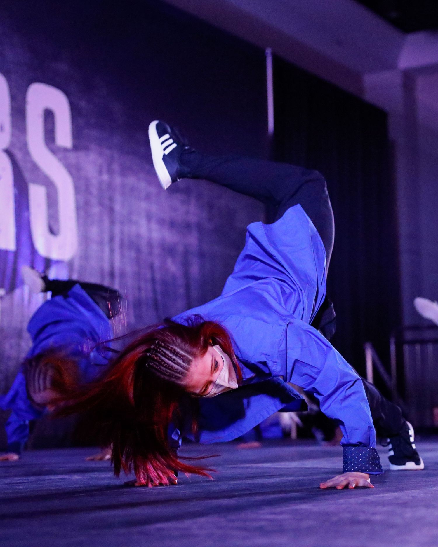 A breakdancer performs a dynamic freeze pose on the floor in a dimly lit space with purple lighting.