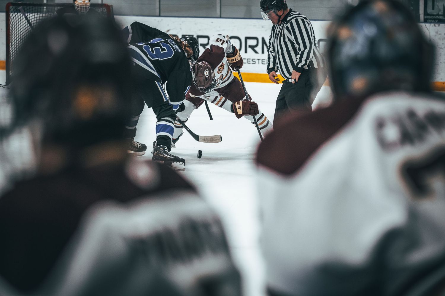 Hockey players compete for the puck during an intense game with referees watching from the side.