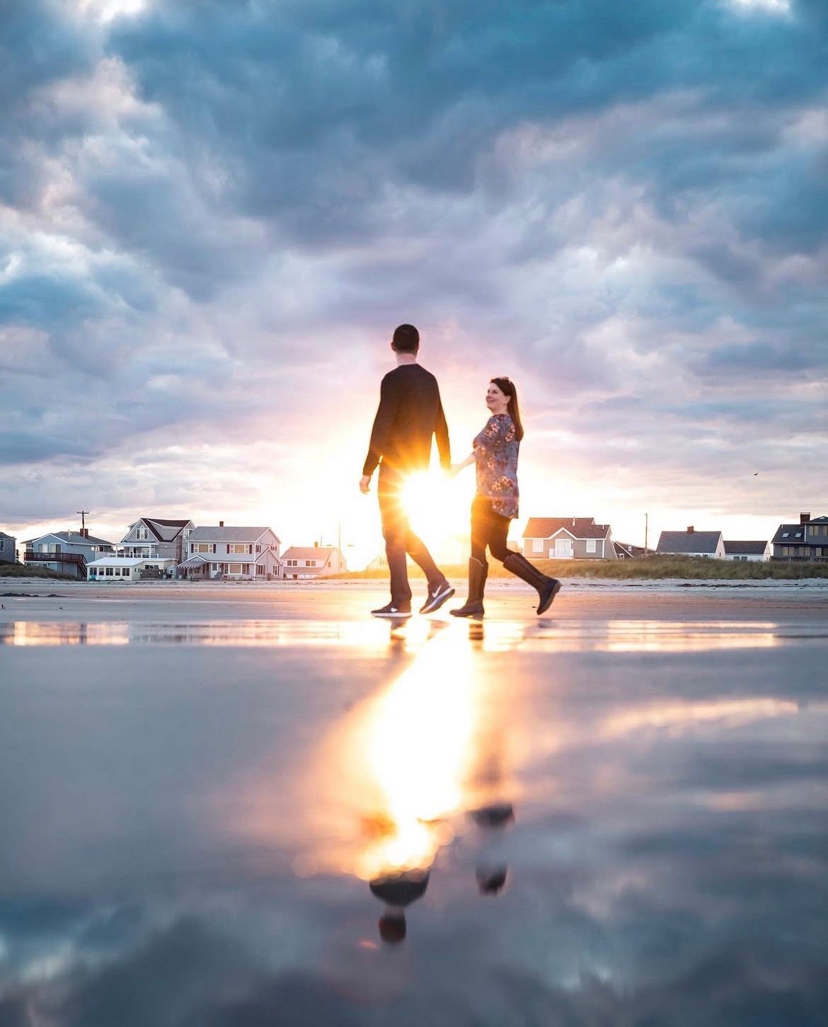 Silhouettes walking on reflective beach surface during dramatic sunset.