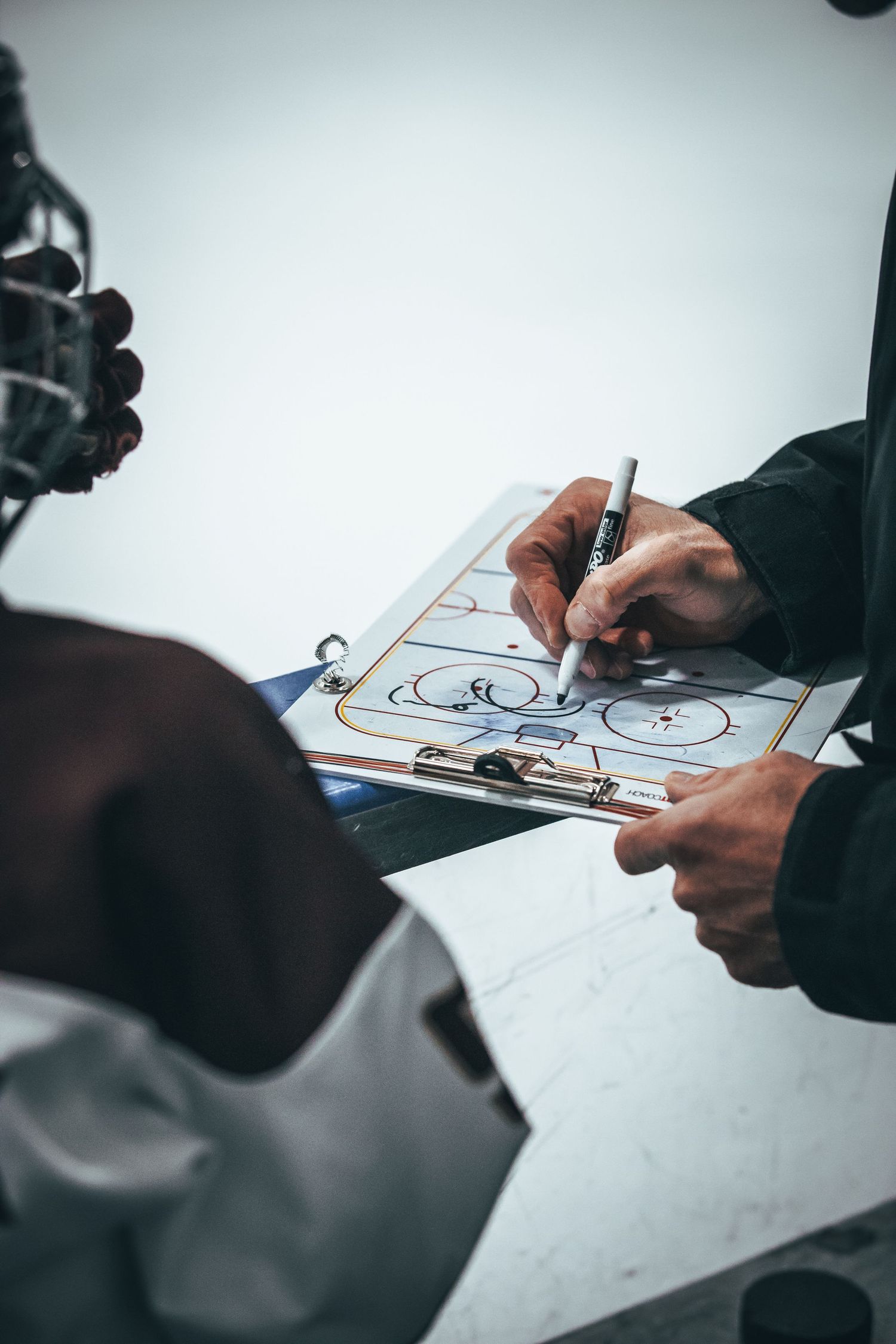 Coach drawing up a sports play diagram on a clipboard during a game or practice session.