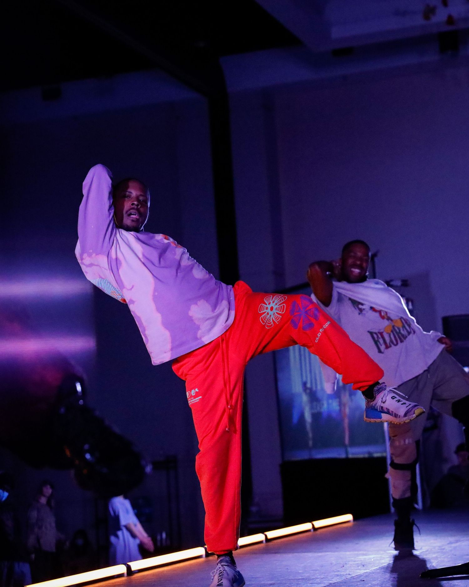 Breakdancer performs an athletic move on stage with dramatic purple and red lighting effects.