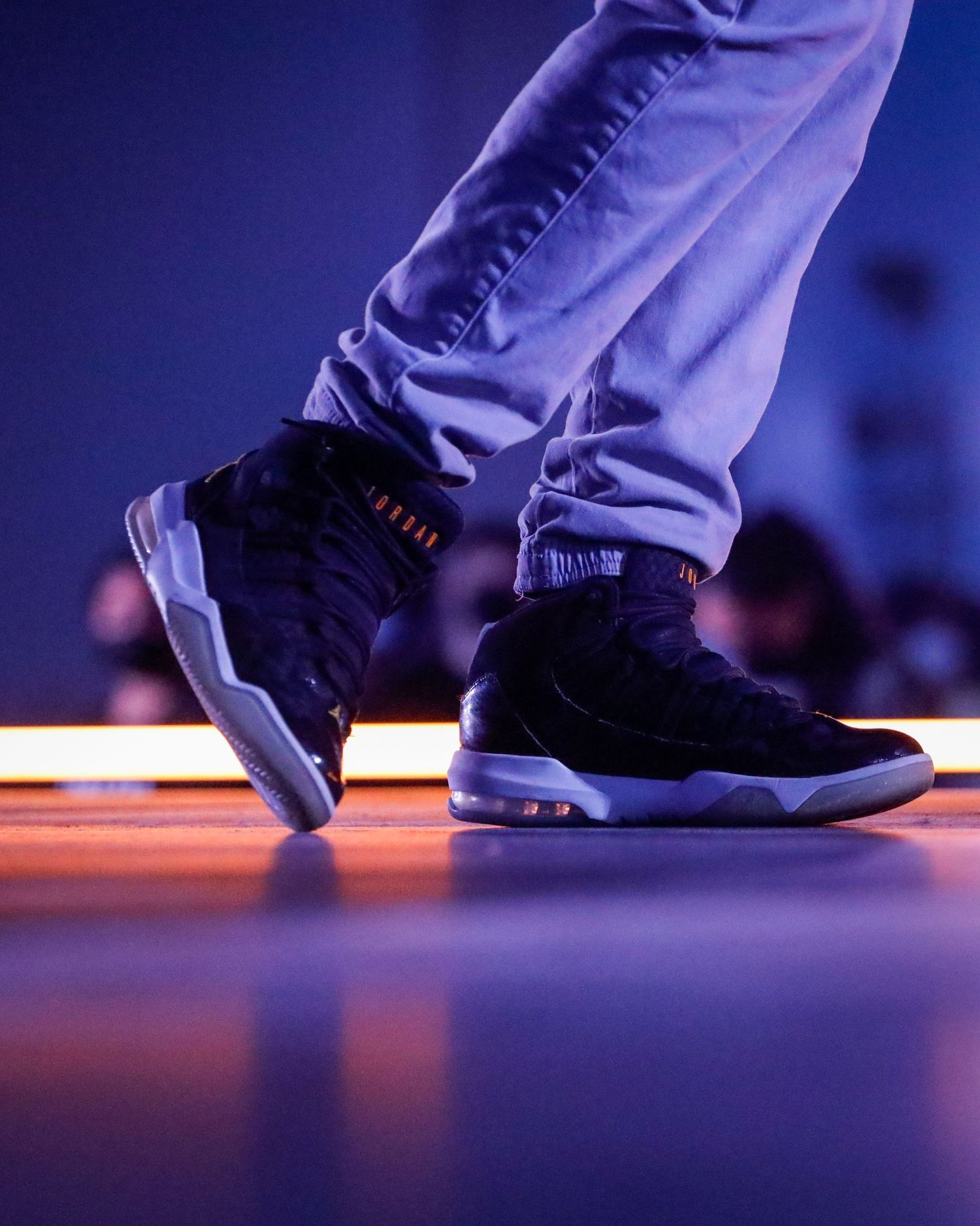 Black Air Jordan 11 sneakers illuminated by purple lighting on a dark stage floor during a stylish footwear shoot.