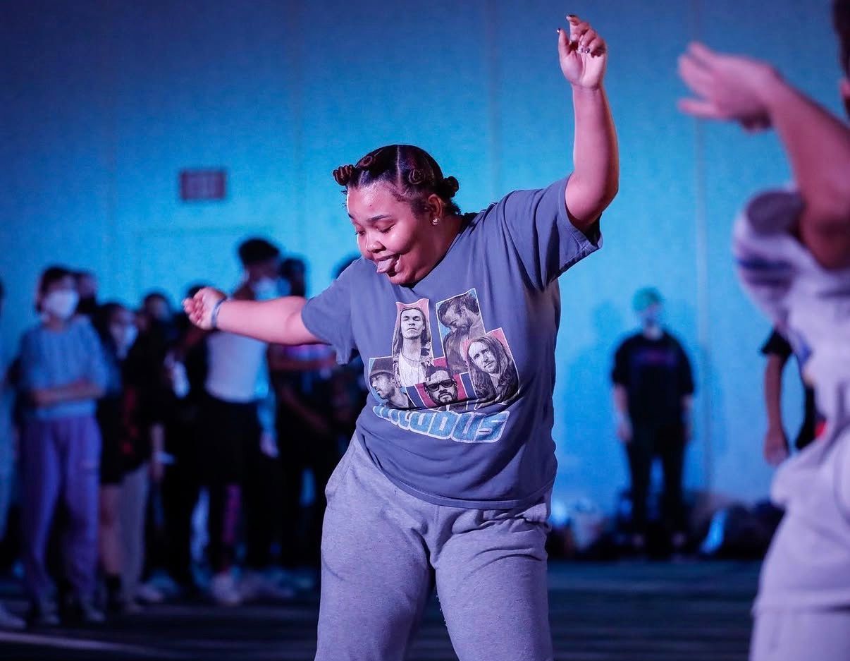 People dancing energetically at a social gathering with blue lighting in the background.