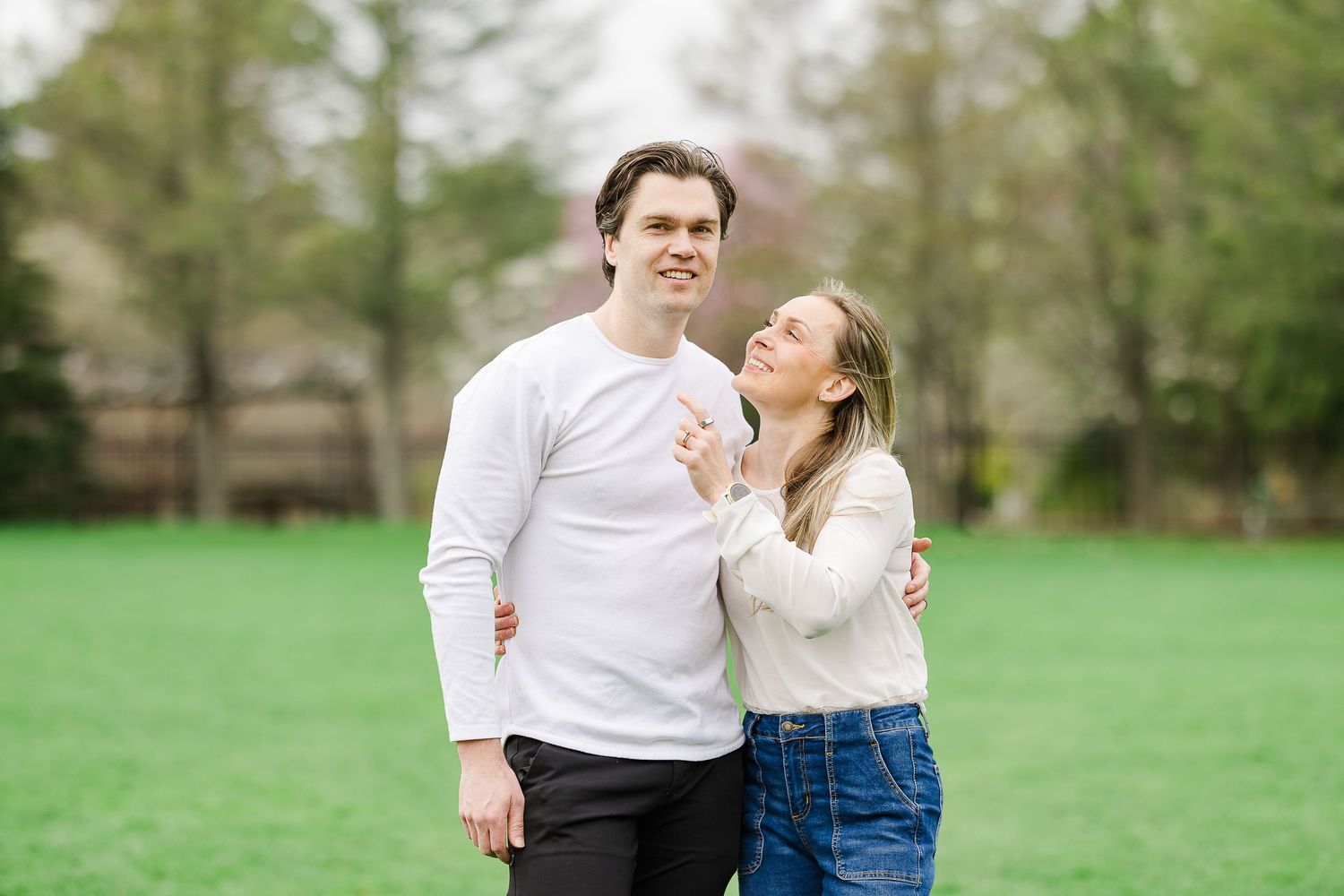 A happy couple in white tops embraces on a green lawn, smiling together outdoors in a park setting.