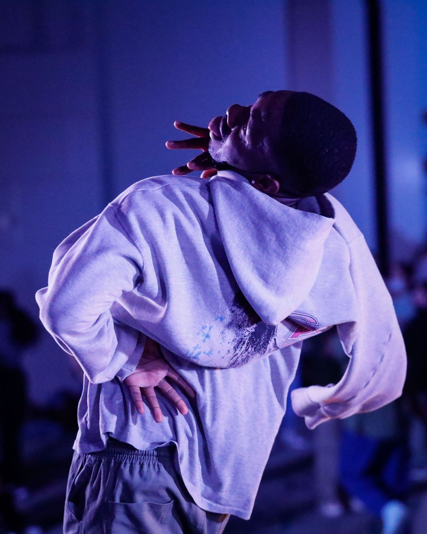 Dancers in white clothing perform a synchronized dance routine in a dimly lit venue with purple lighting.