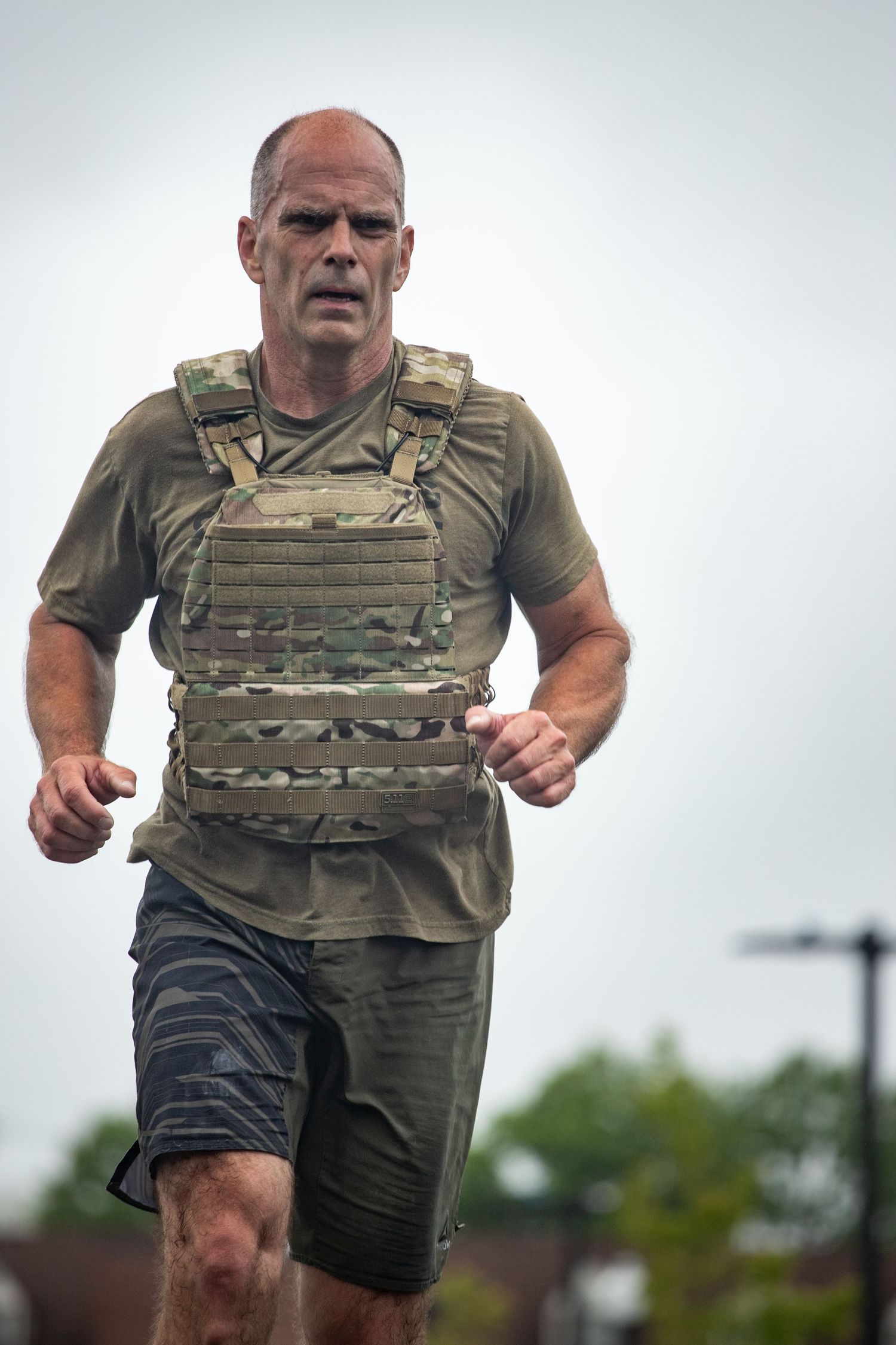 A person wearing tactical gear performs an intense workout in an outdoor setting.