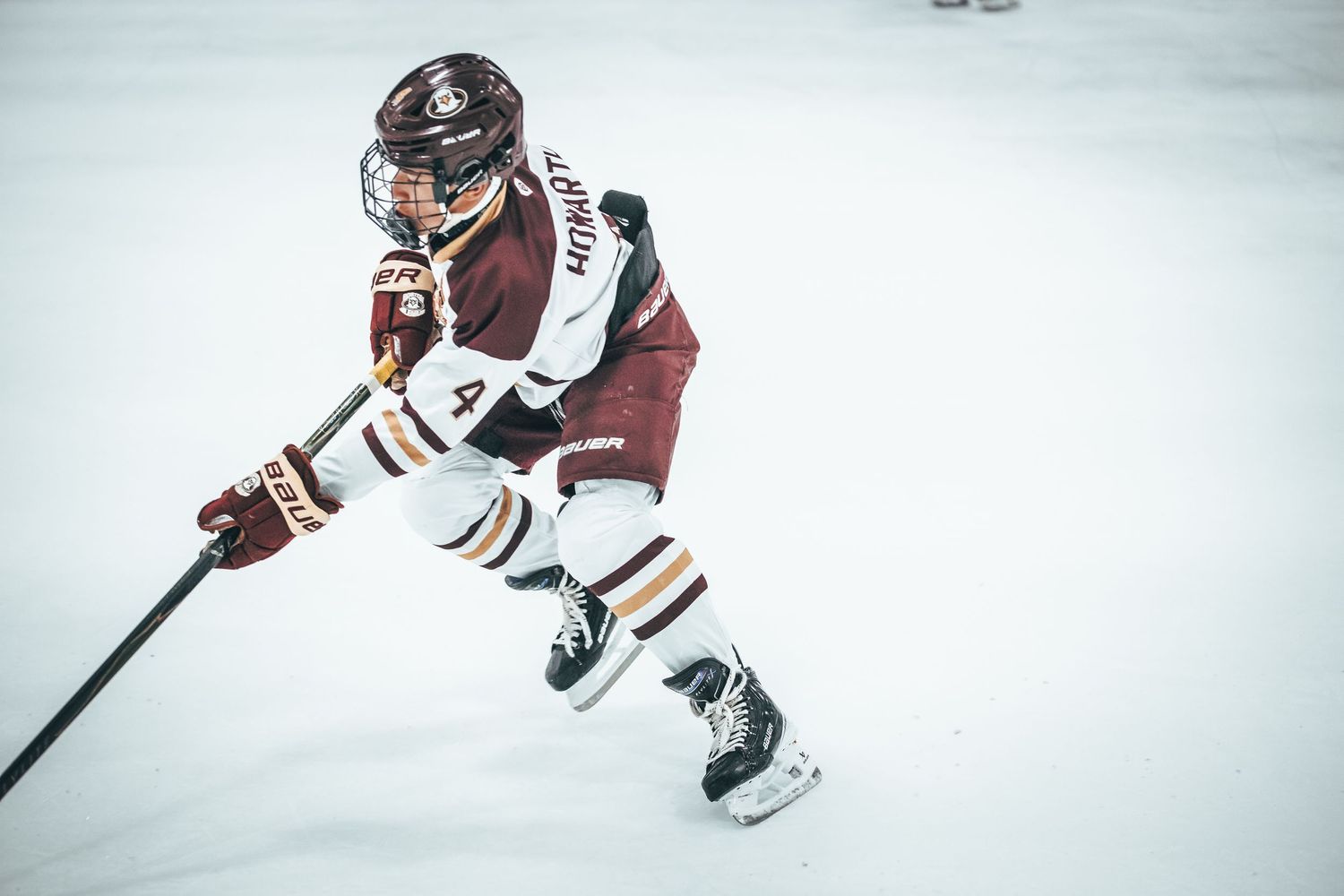 Hockey player in maroon jersey carries puck down ice during competitive game action.