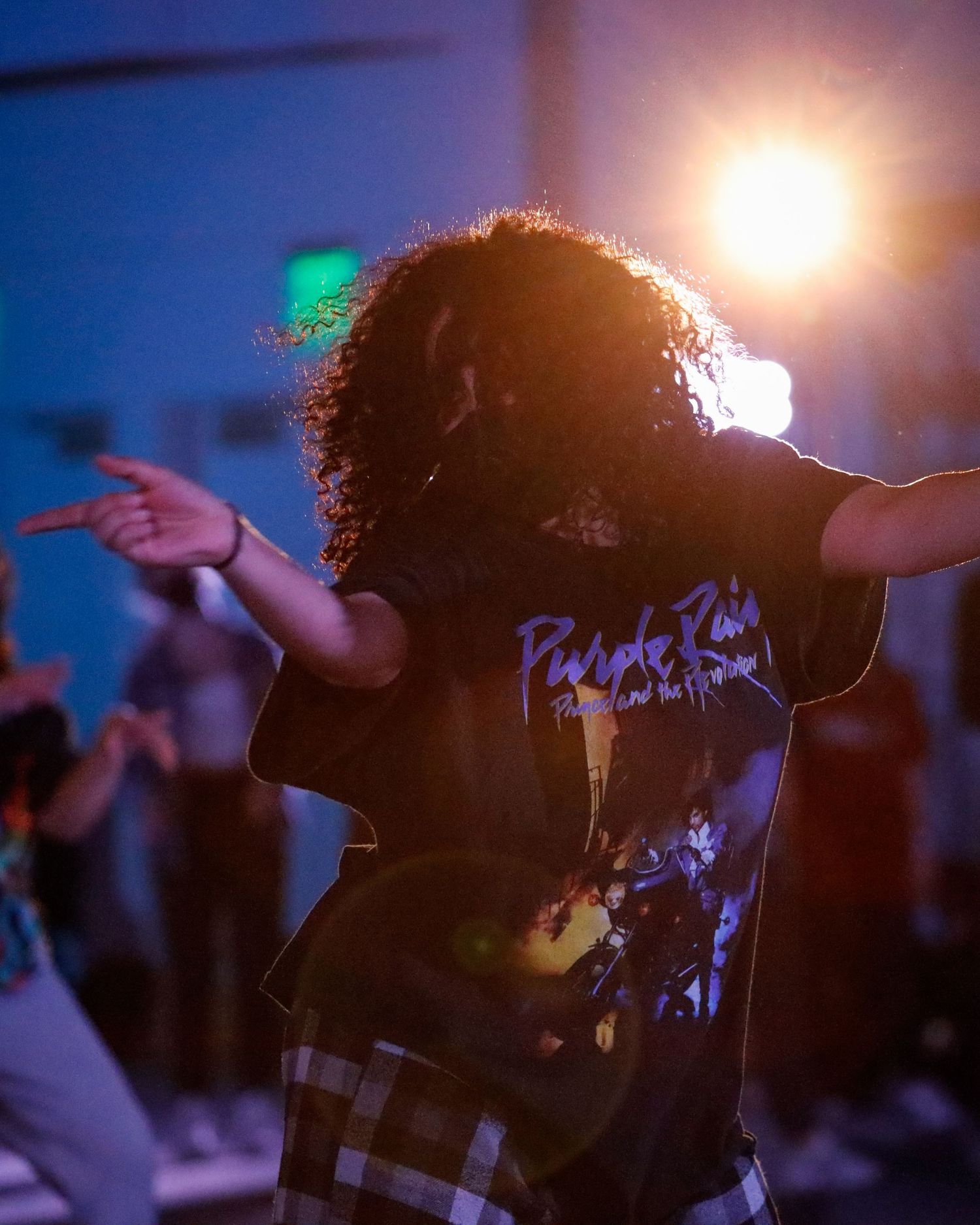 A silhouetted figure dances against a backlit stage with dramatic lighting creating a glowing halo effect.