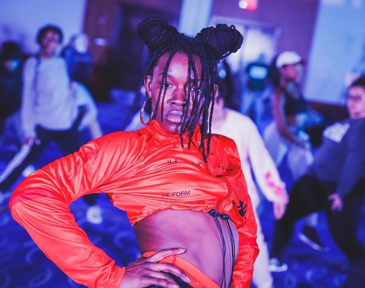 Dancer in red jacket performs with dramatic pose under atmospheric lighting.