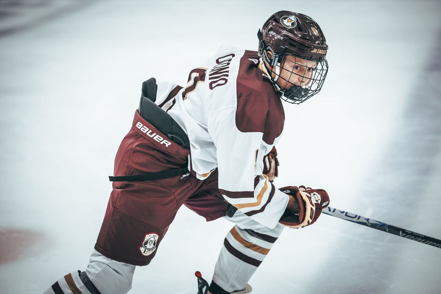 Hockey players in maroon and white jerseys battle for the puck during an intense game on the ice.
