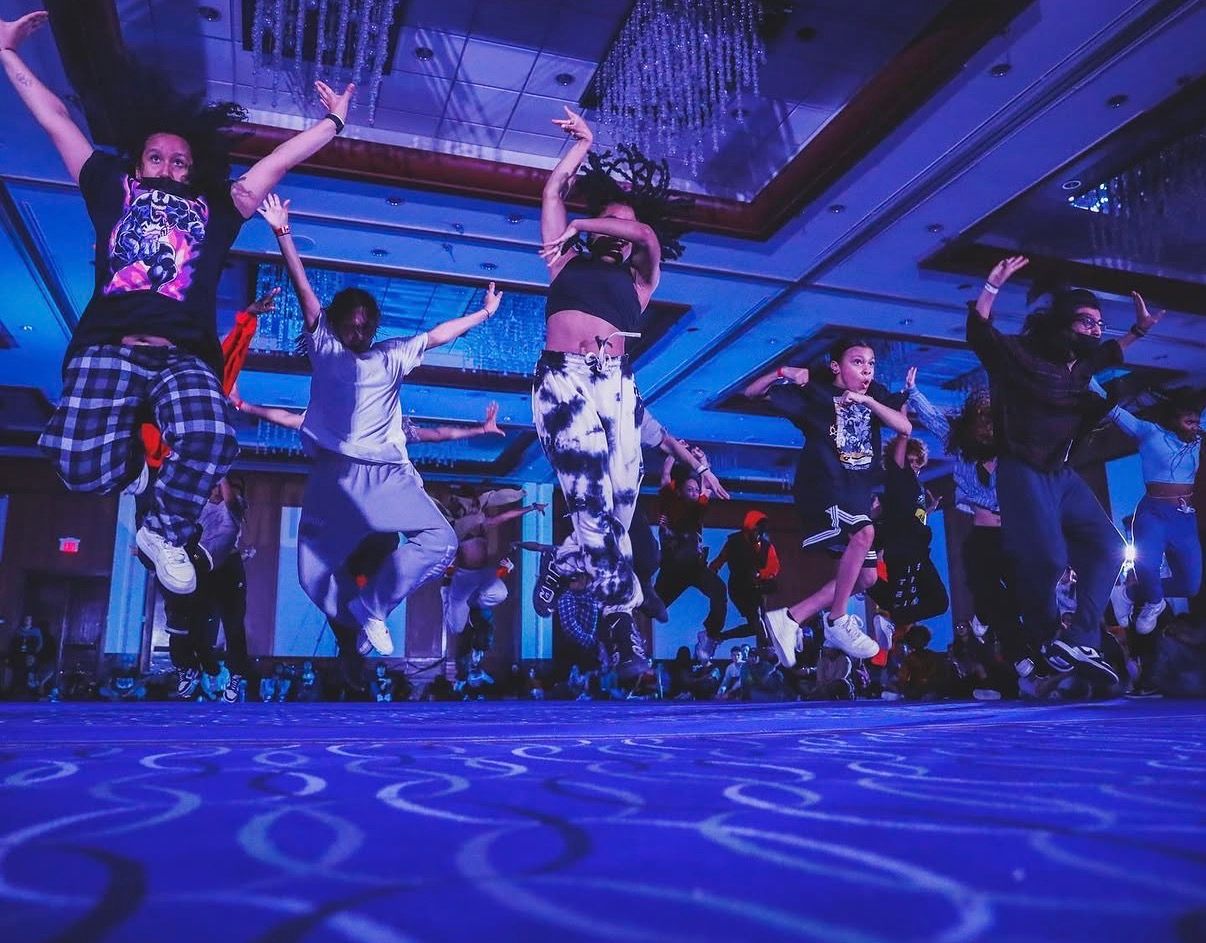 Dancers perform energetic moves under blue and purple stage lighting during a dynamic dance performance.