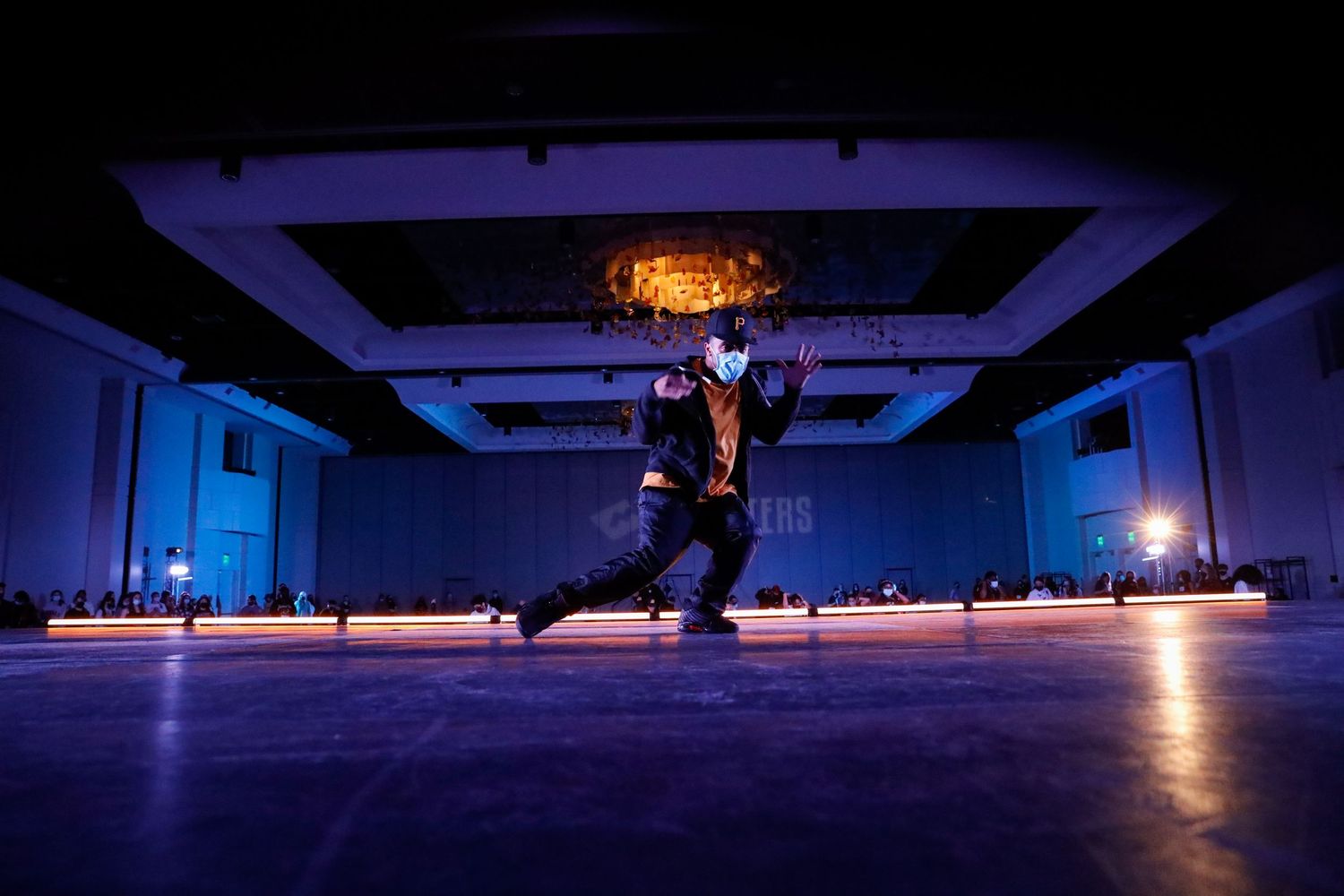 Panoramic view of an empty ballroom with dramatic blue lighting and ornate chandeliers creating a moody atmosphere.