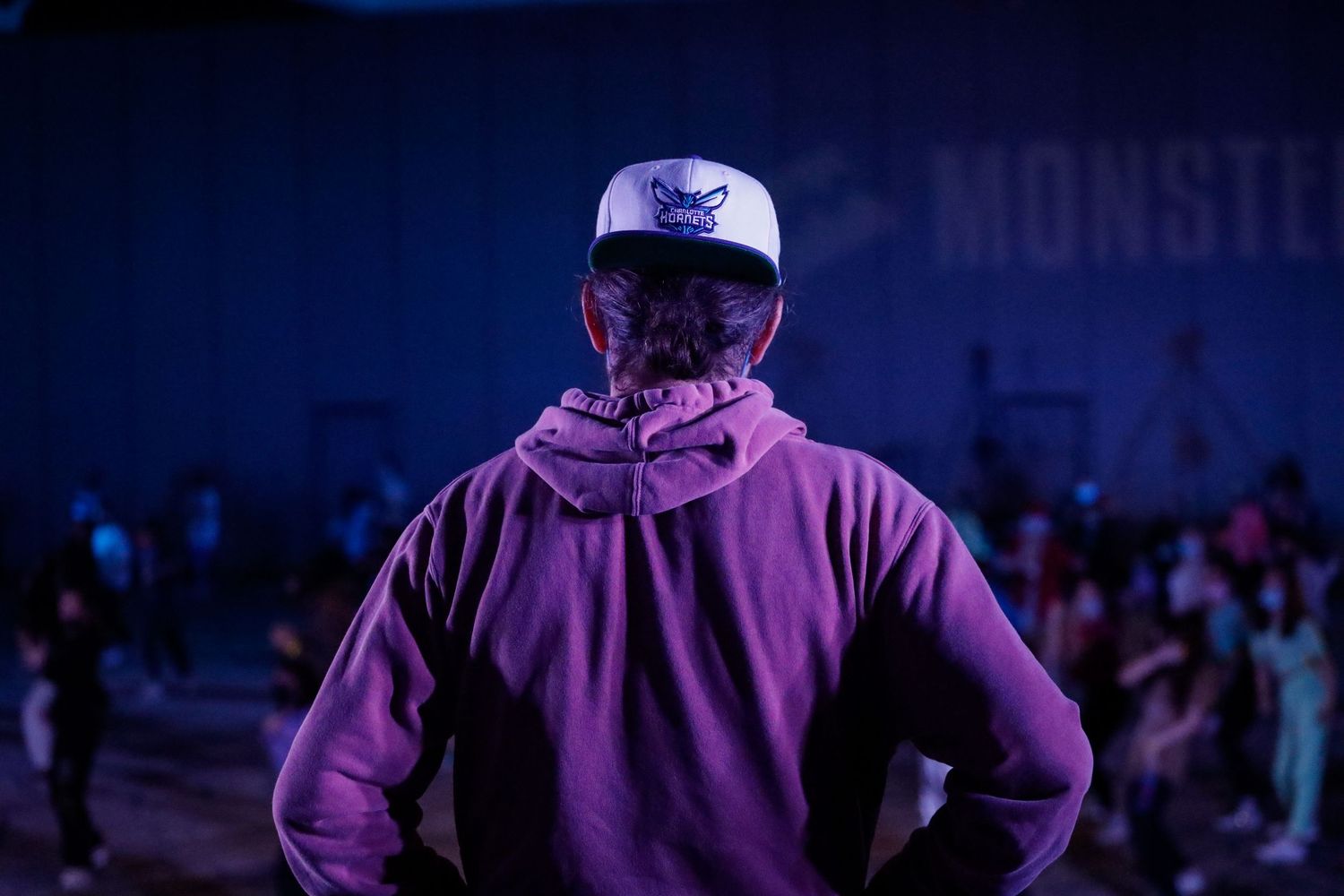 Concert performer in purple hoodie stands on stage with dramatic blue lighting and crowd in background.