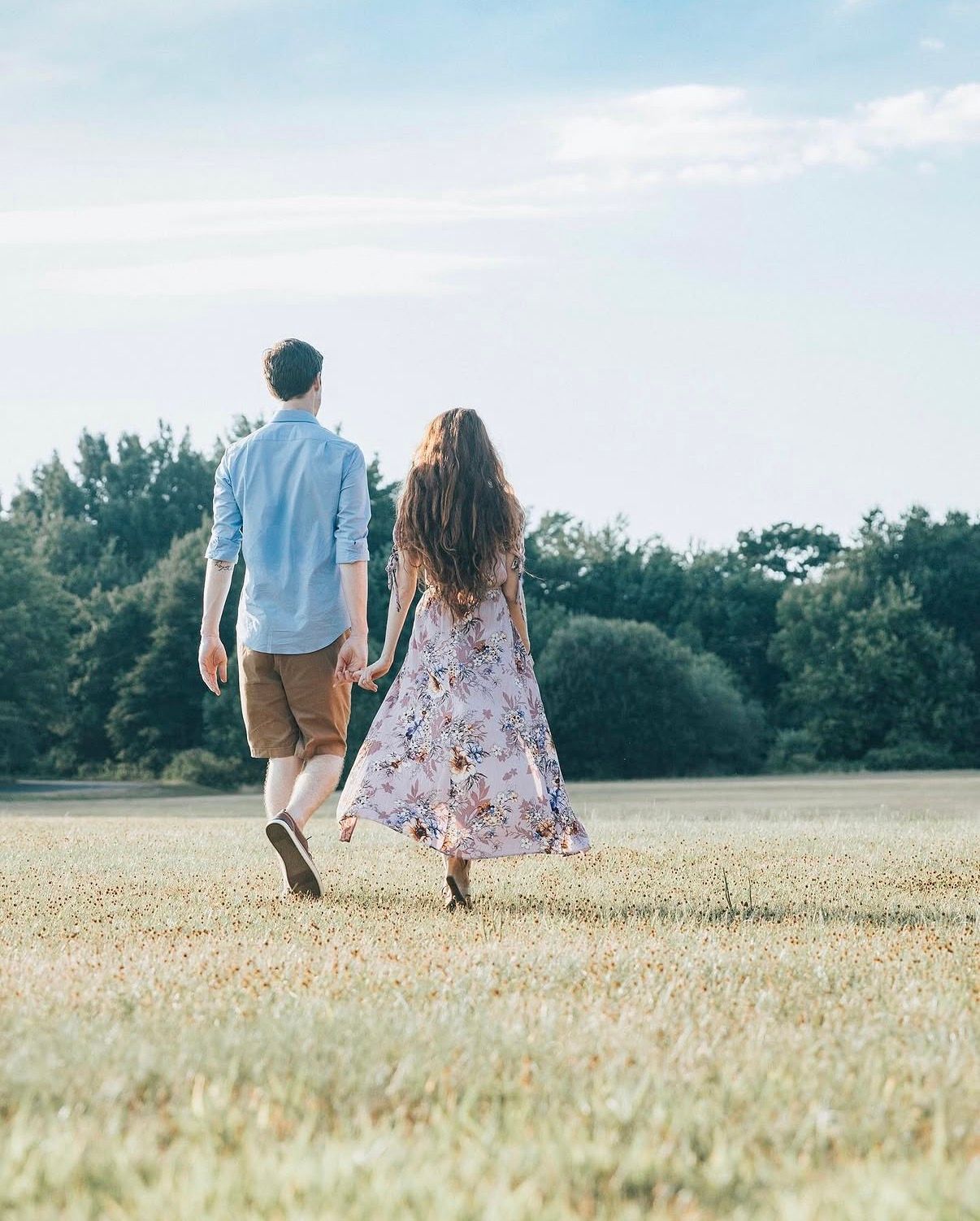 A couple walks hand in hand through a golden wheat field on a sunny summer day.