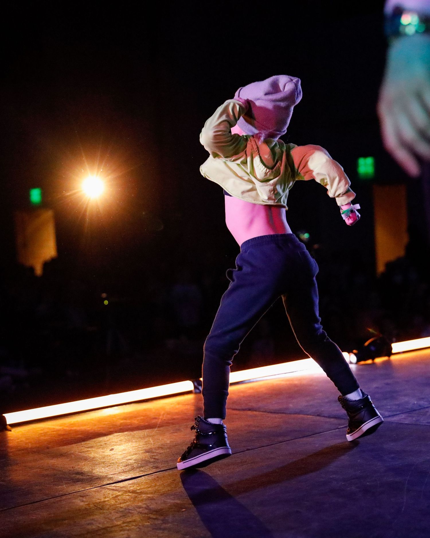 A dancer performs a dramatic breakdancing move on a dimly lit stage with dramatic lighting effects.
