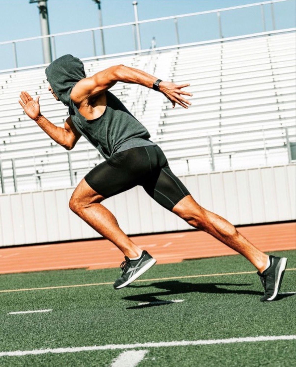Athlete in sleeveless hoodie demonstrating explosive sprint start position on track field.