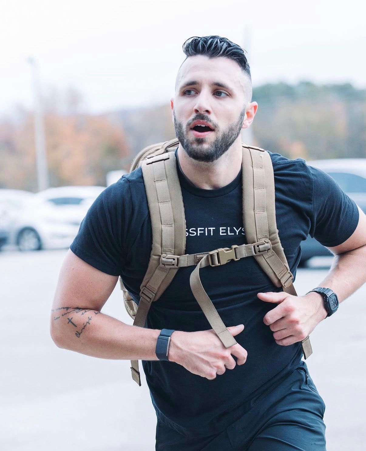 Athlete wearing black t-shirt and tan backpack demonstrates proper posture for fitness training.