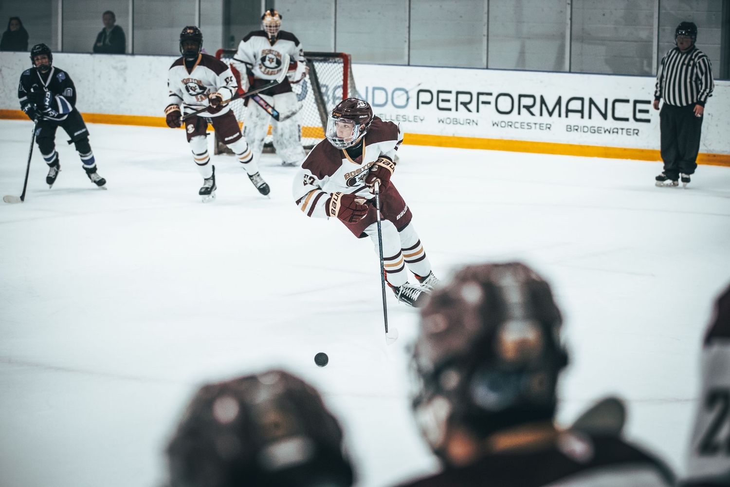 Hockey players chase after the puck during an intense game with Pro Performance signage visible in the background.