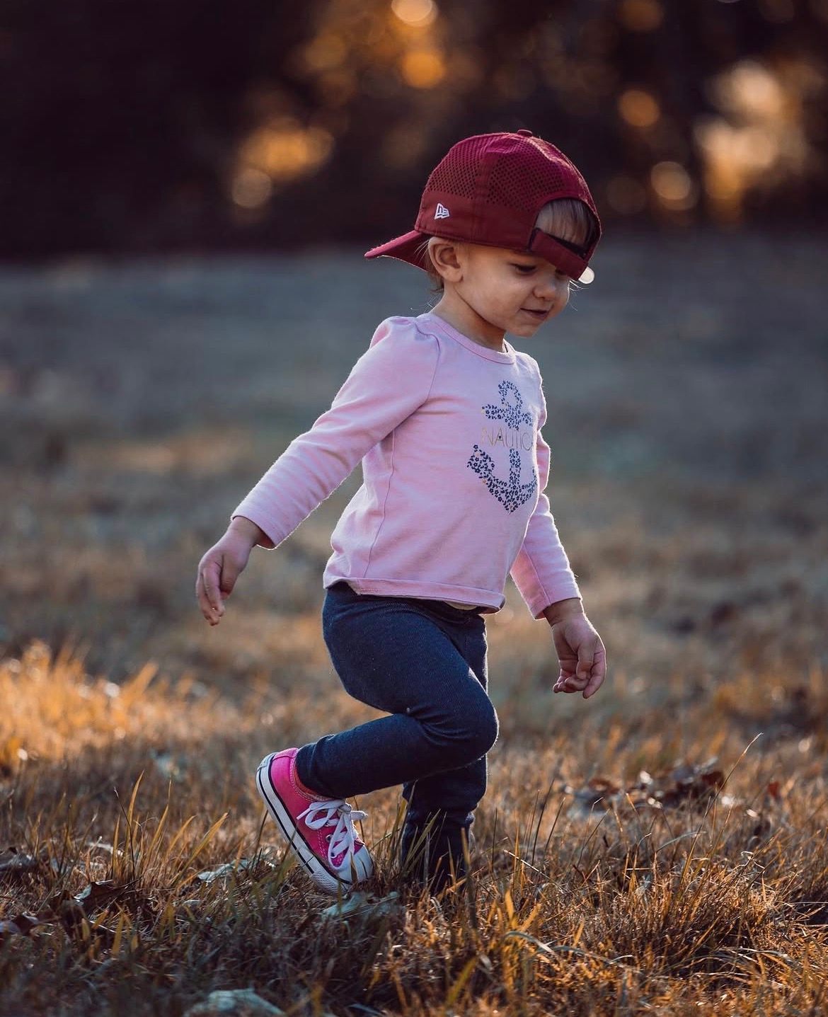 Child in pink shirt and baseball cap playing in golden evening light.