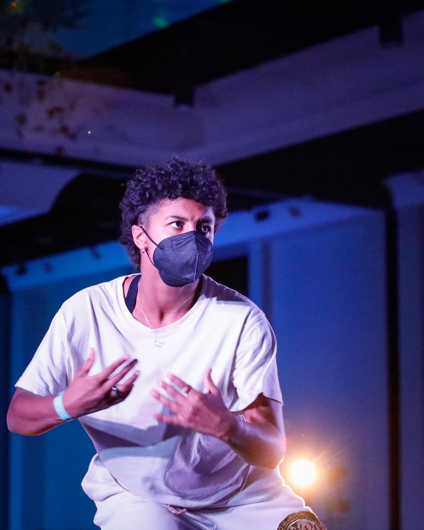 A performer in a white t-shirt dances expressively against a dark background with dramatic blue lighting.