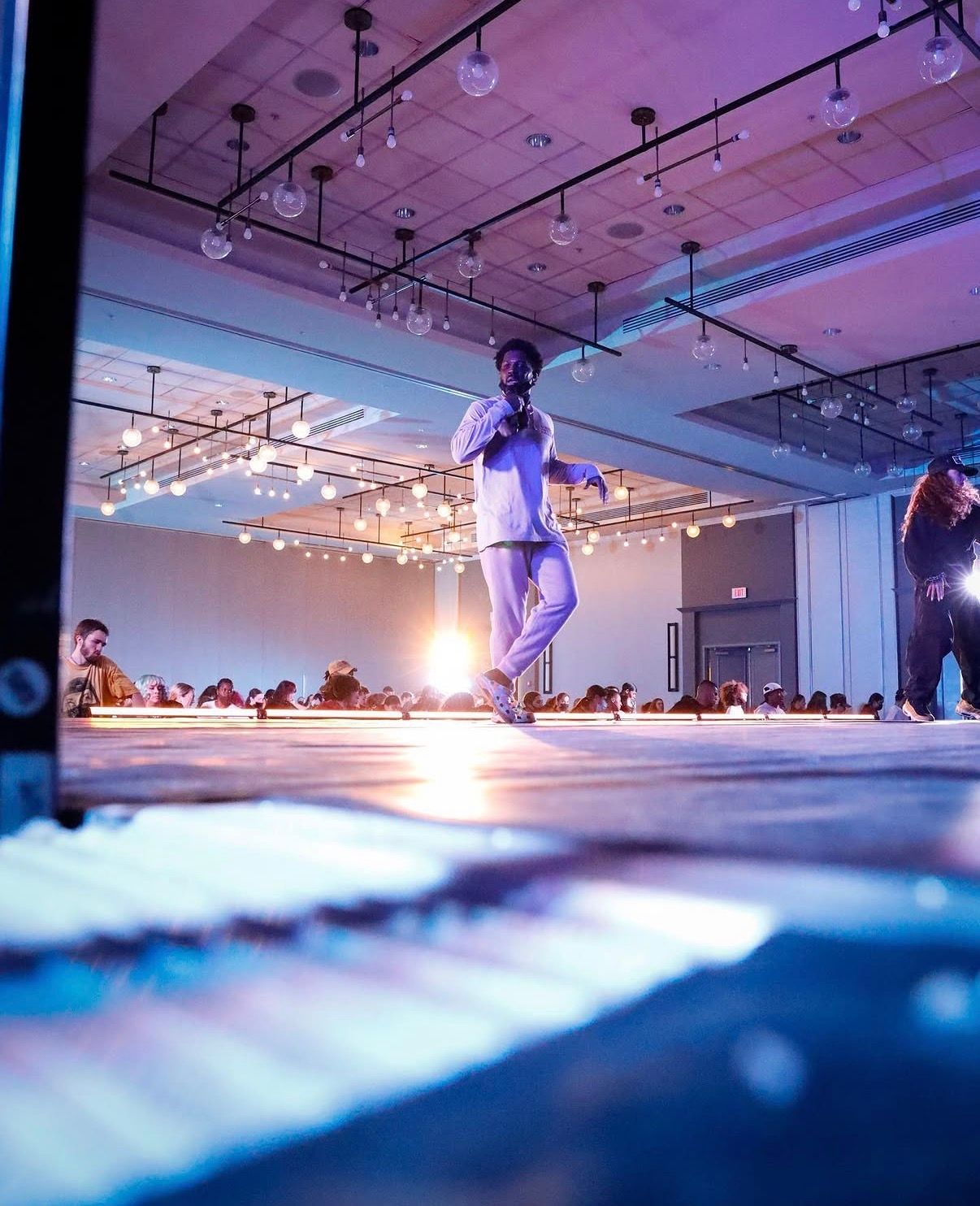 Artistic fashion show runway with blue lighting and silhouetted figures casting long shadows in a modern gallery space.