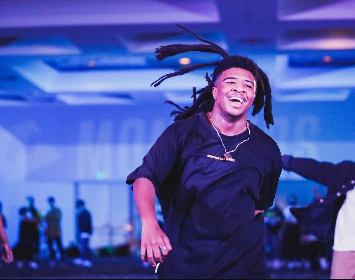 Dancer in black attire moves expressively during indoor performance with blue lighting.