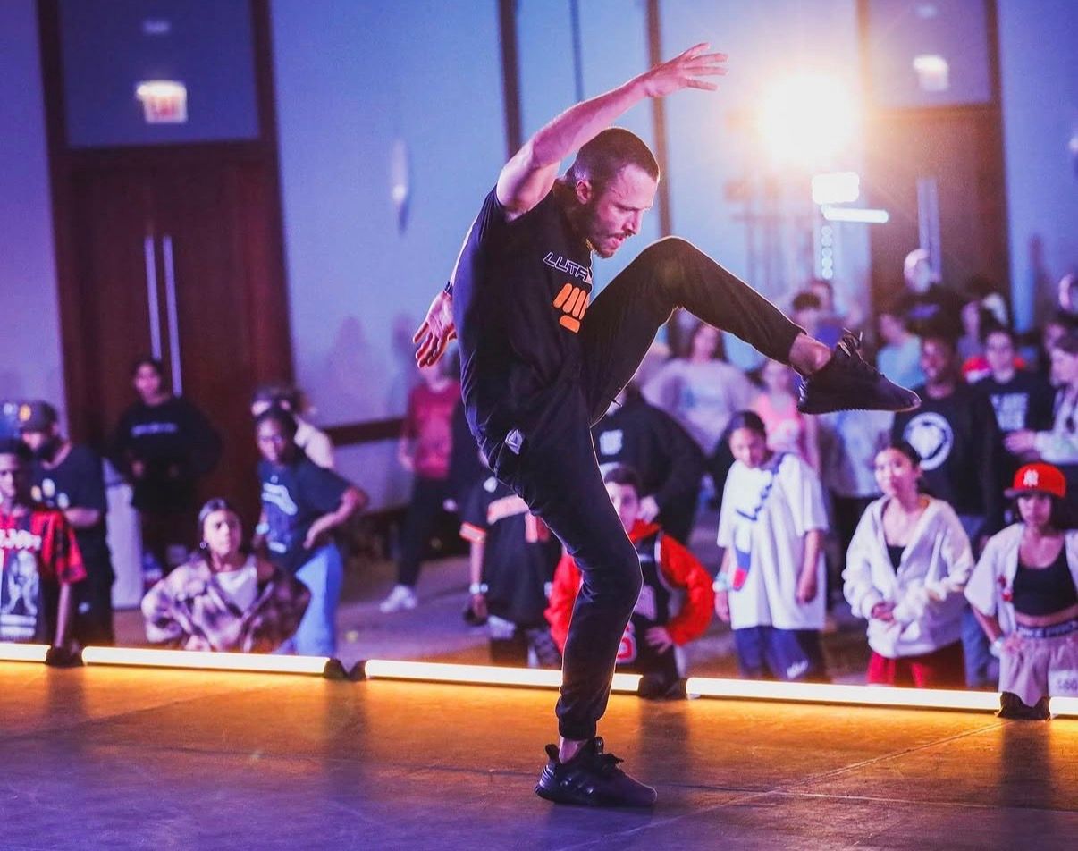 Break dancers perform dynamic floor moves during a competition with colorful stage lighting in the background.