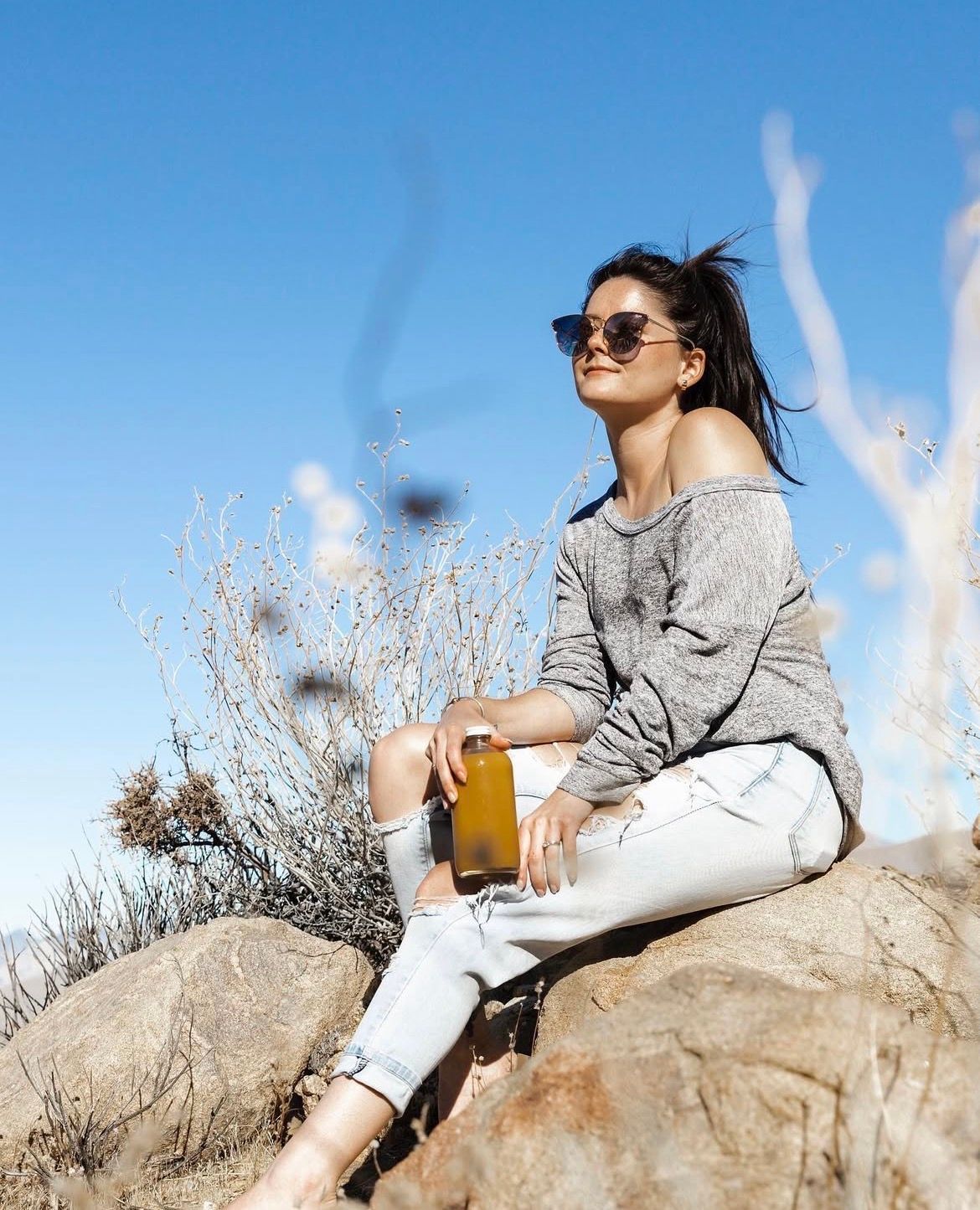 Person in casual wear relaxing on rocky terrain with beverage.
