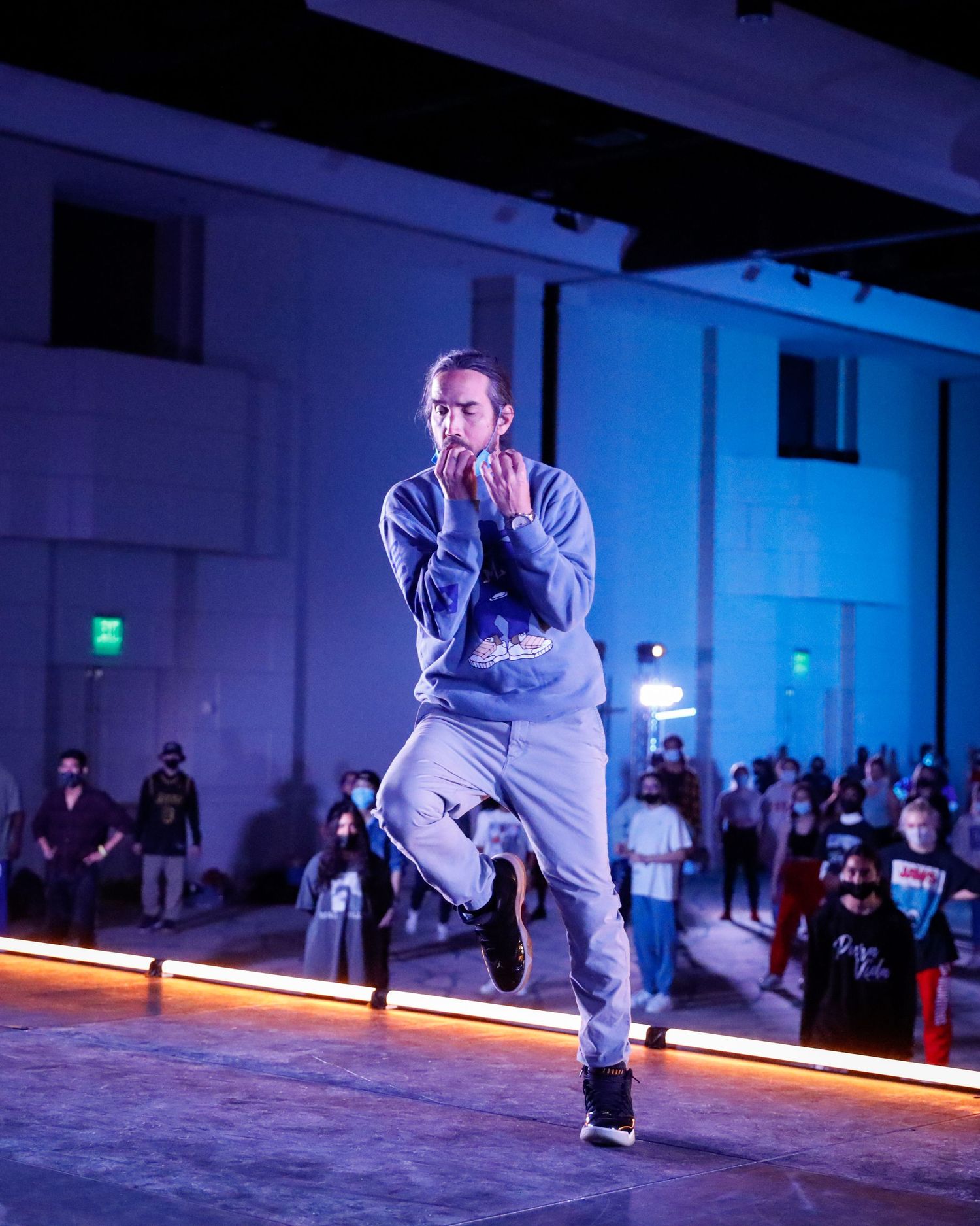 A dancer performs a dynamic breakdancing move in a dimly lit performance space with blue lighting.
