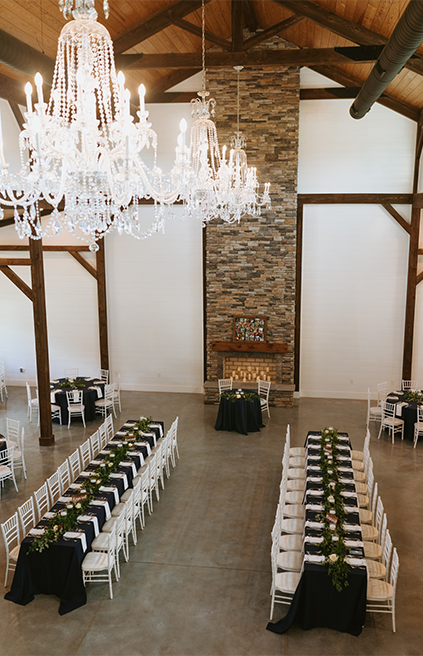 Elegant wedding reception venue with crystal chandeliers and long banquet tables decorated with black linens and greenery.