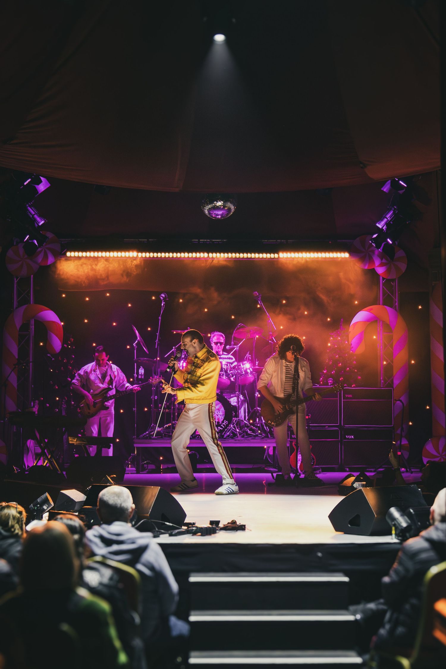 Wide concert stage shot with performer in white outfit against vibrant purple and pink lighting effects.