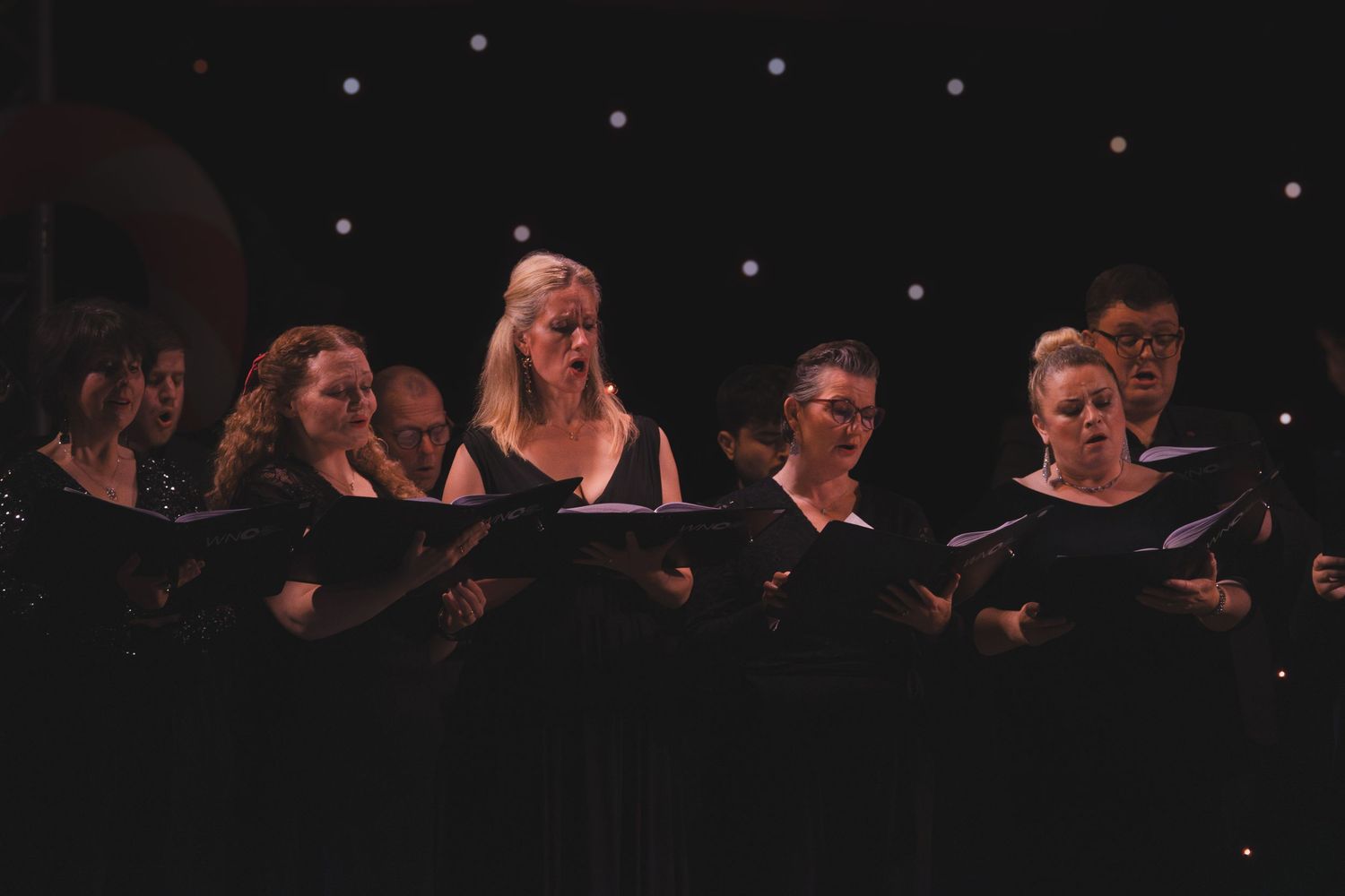 Choir members performing on stage with blue accent lights in the background.