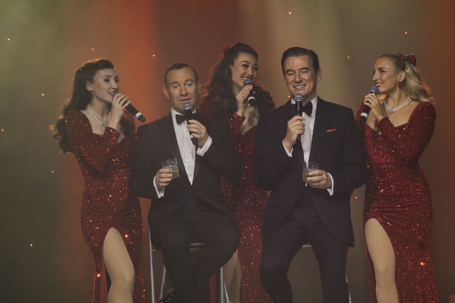 A group of entertainers perform together in formal wear on stage.
