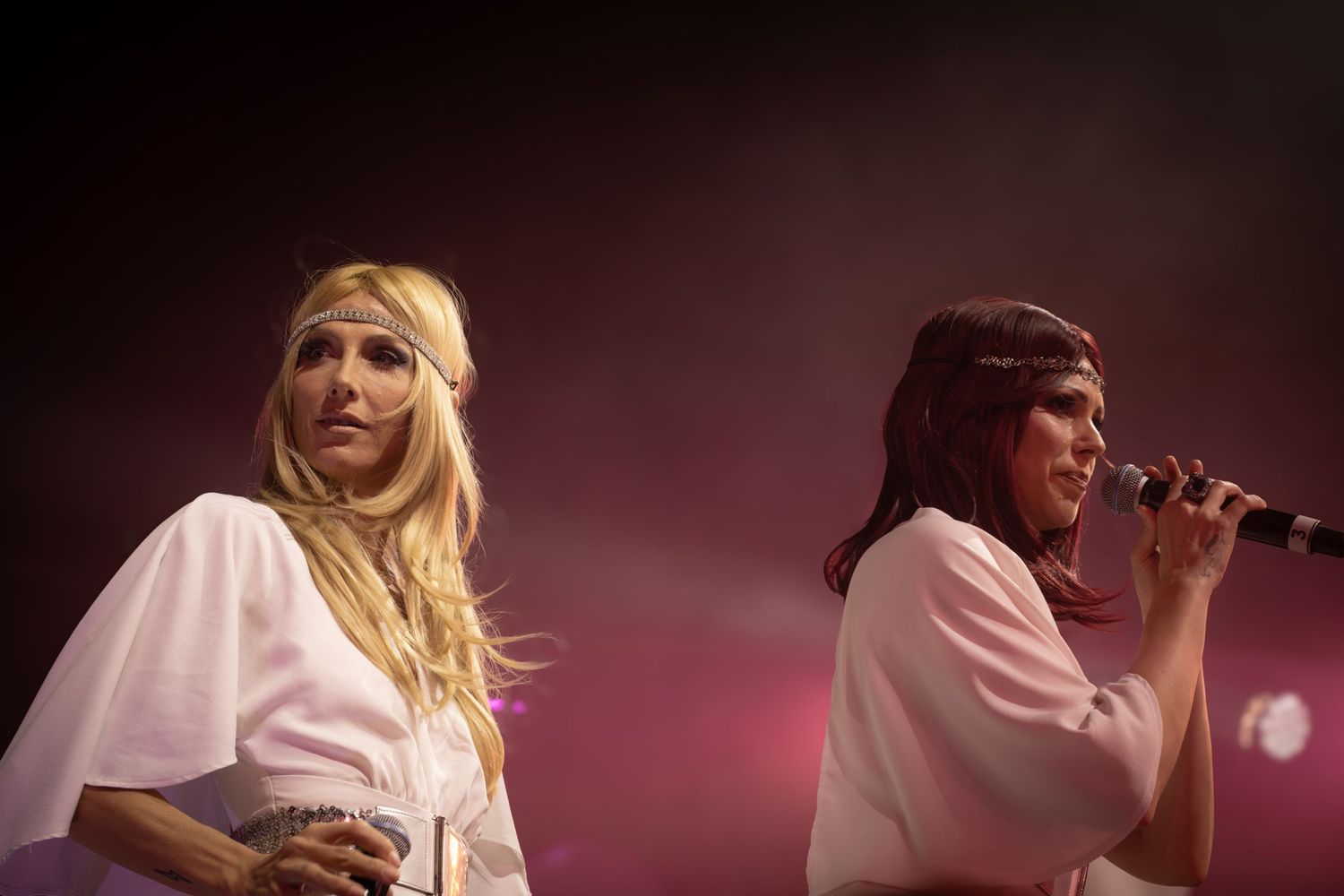Performer in white dress delivers emotional performance under dramatic stage lighting.