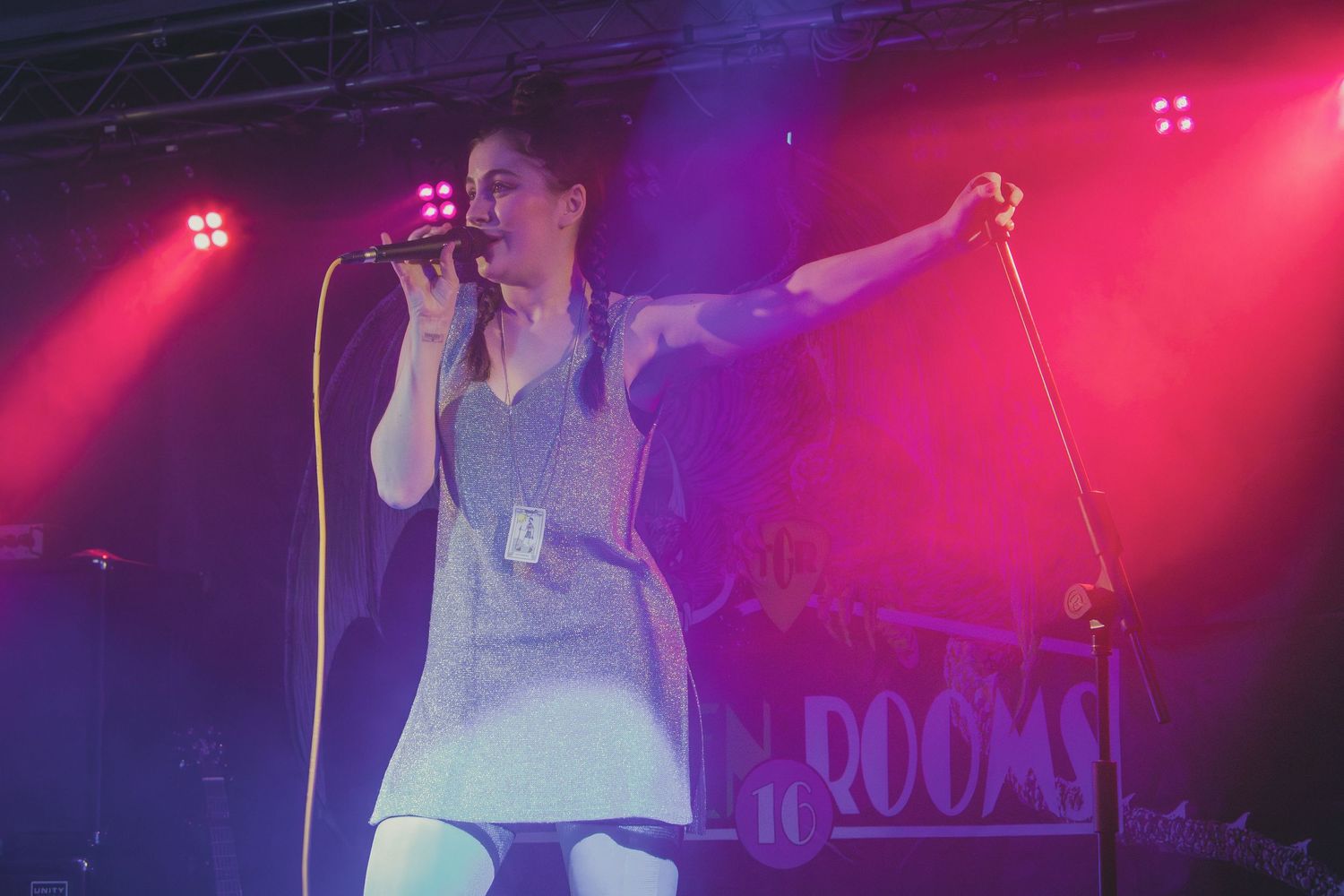 Concert performer singing on stage with dramatic pink and blue lighting effects in a live music venue.